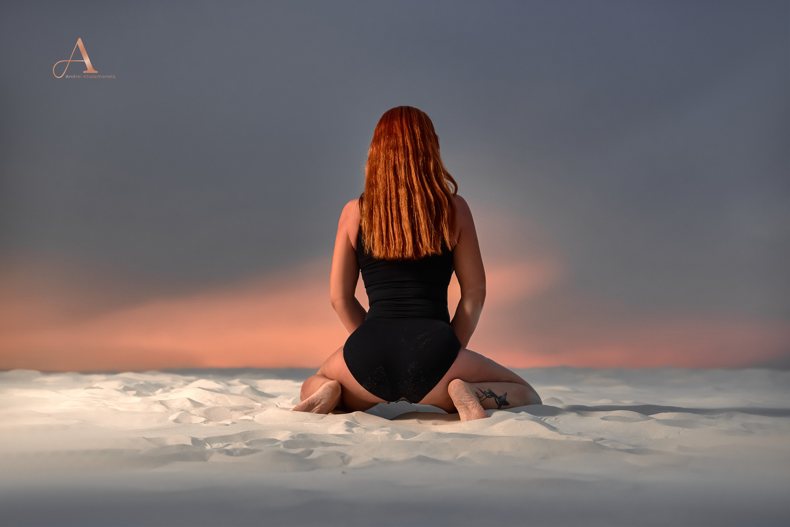 Девушка в черном боди сидит на песке, вид со спины, фотосессия на закате.