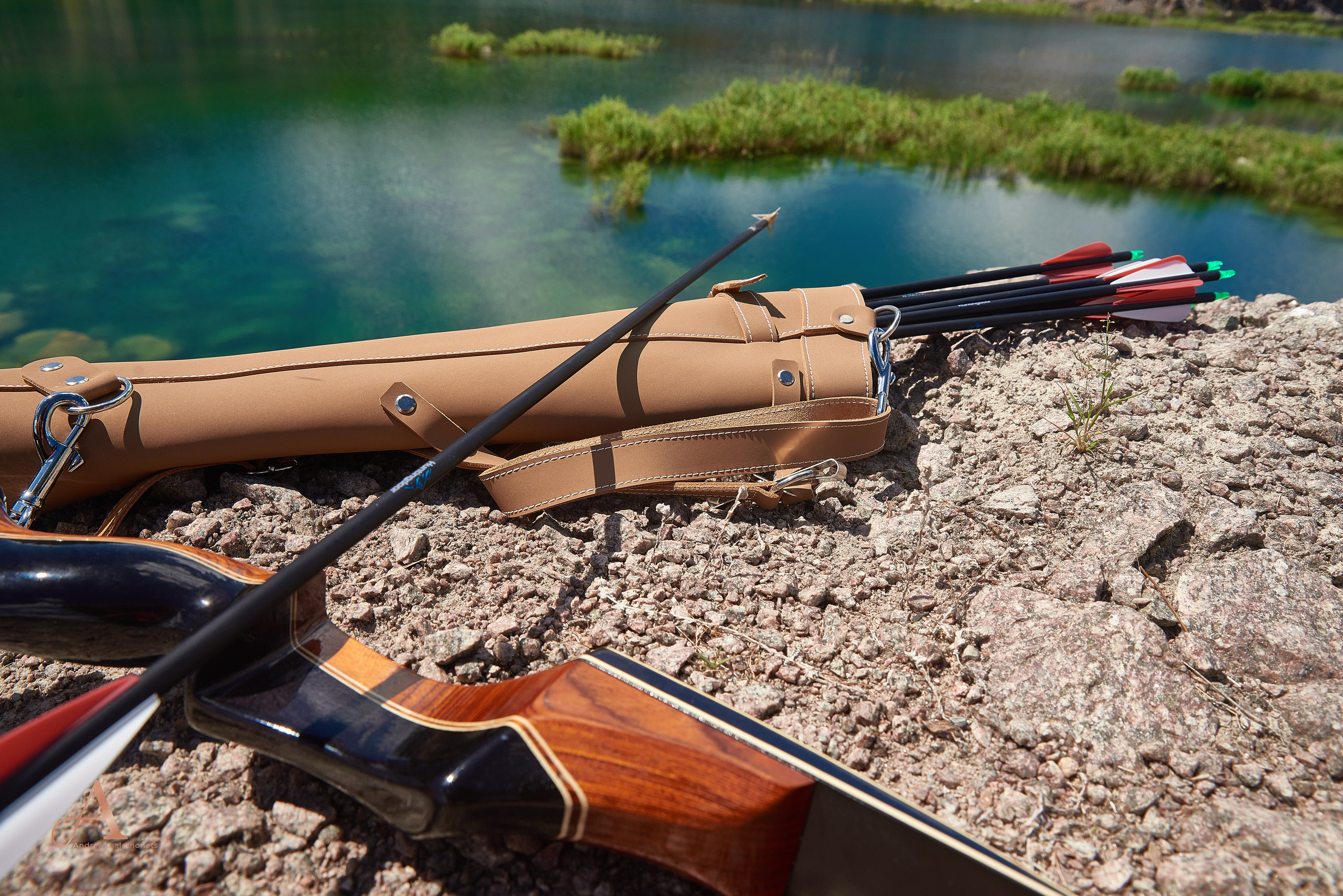 Красивый деревянный охотничий лук и кожаный колчан со стрелами лежат на камнях на фоне озера.