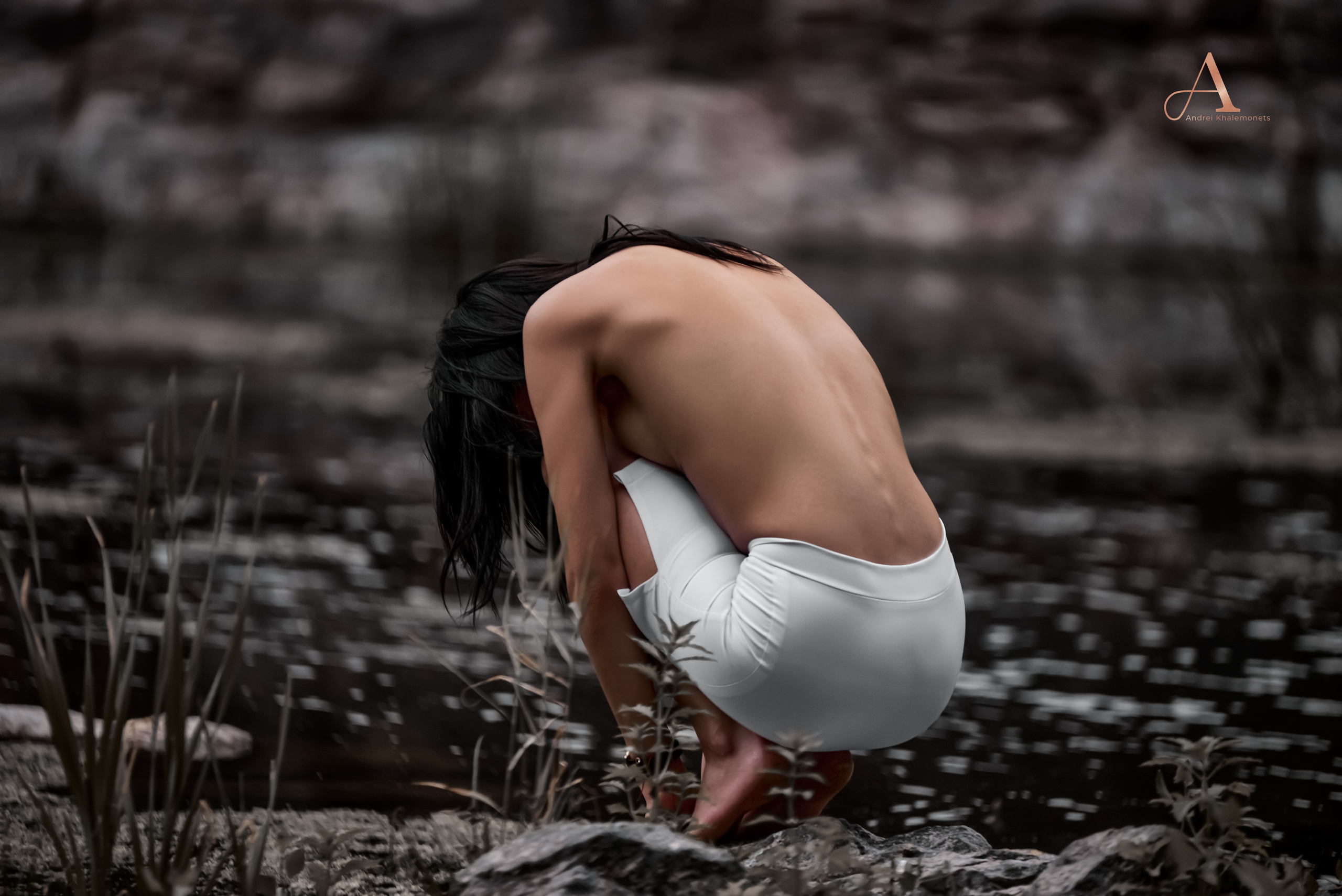 Девушка топлес в белой узкой юбке сидит спиной в кадр на природе у водоема.