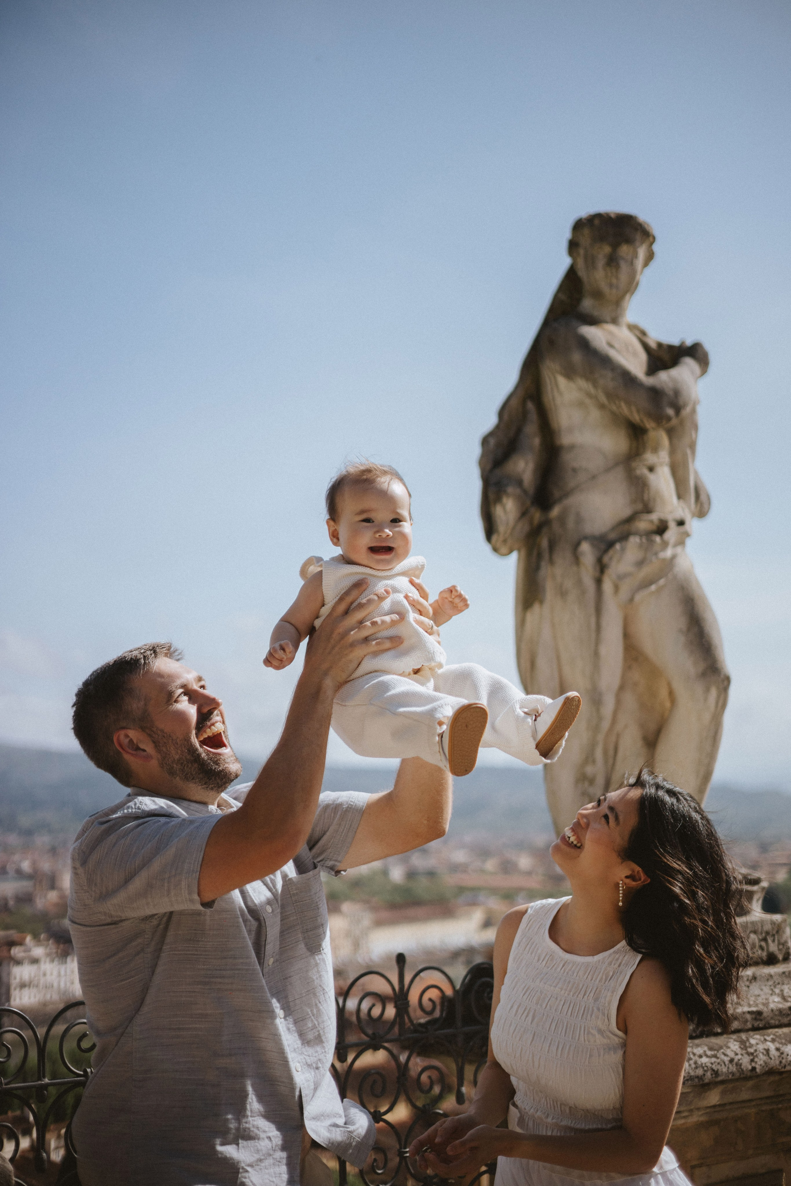 Papà che gioca con la sua bambina durante un servizio fotografico di famiglia a Villa Bardini accanto a una statua storica.