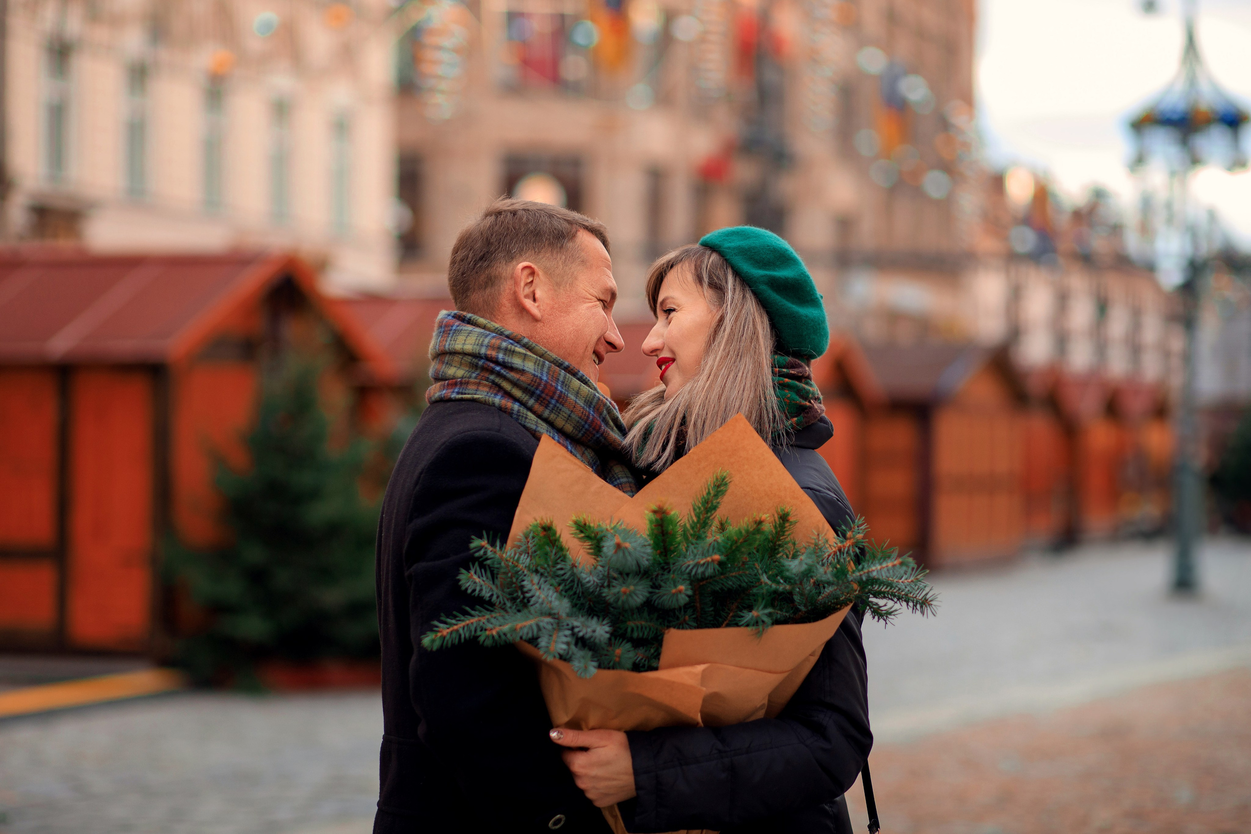 Чоловік та жінка посміхаються і обнімаються, тримають букет з гілками ялинки