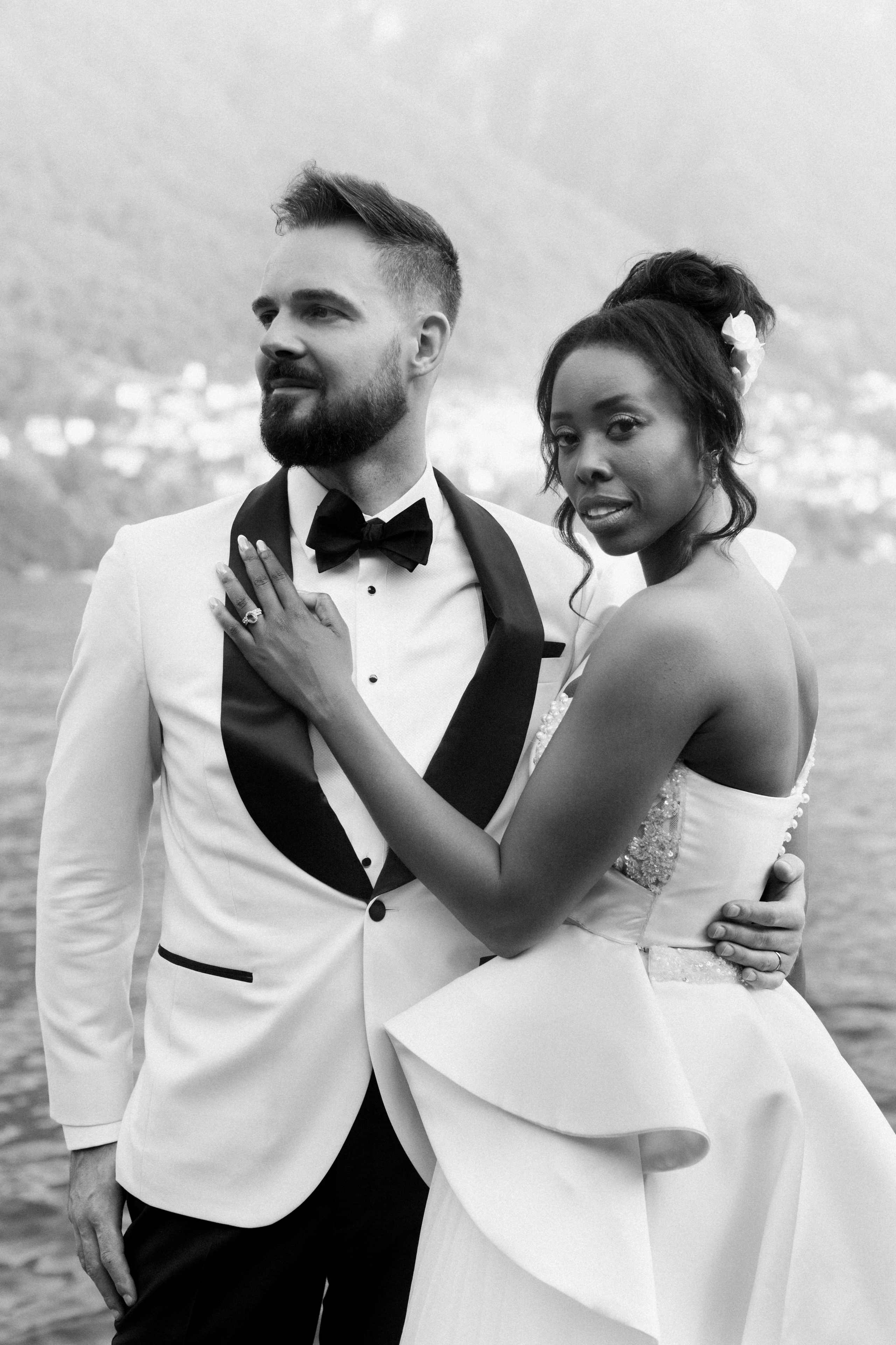 Elegant black-and-white editorial portrait of a couple with scenic Lake Como in the background, highlighting modern wedding fashion