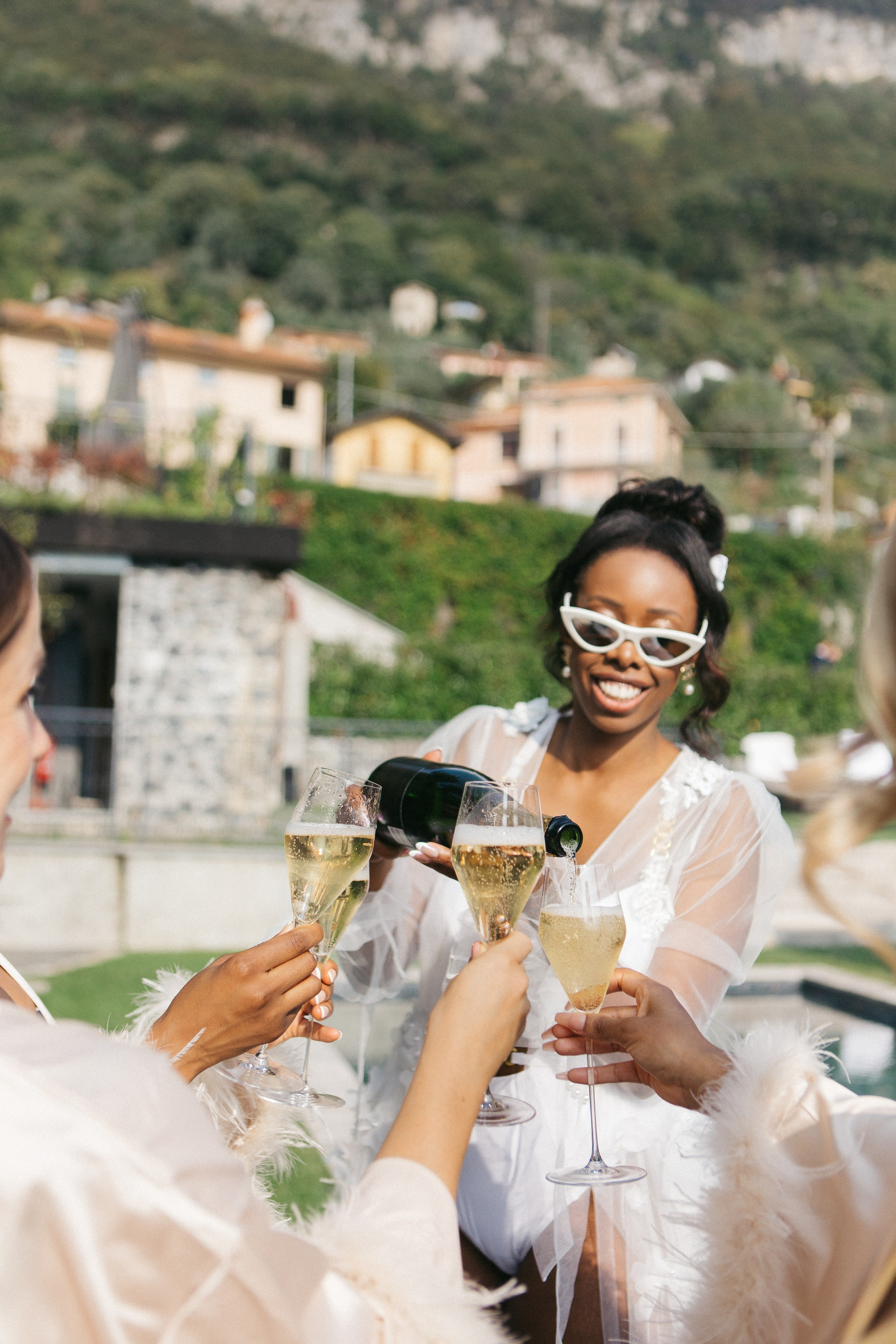 Smiling dark-skinned bride pouring champagne into her bridesmaids’ glasses during a joyful celebration