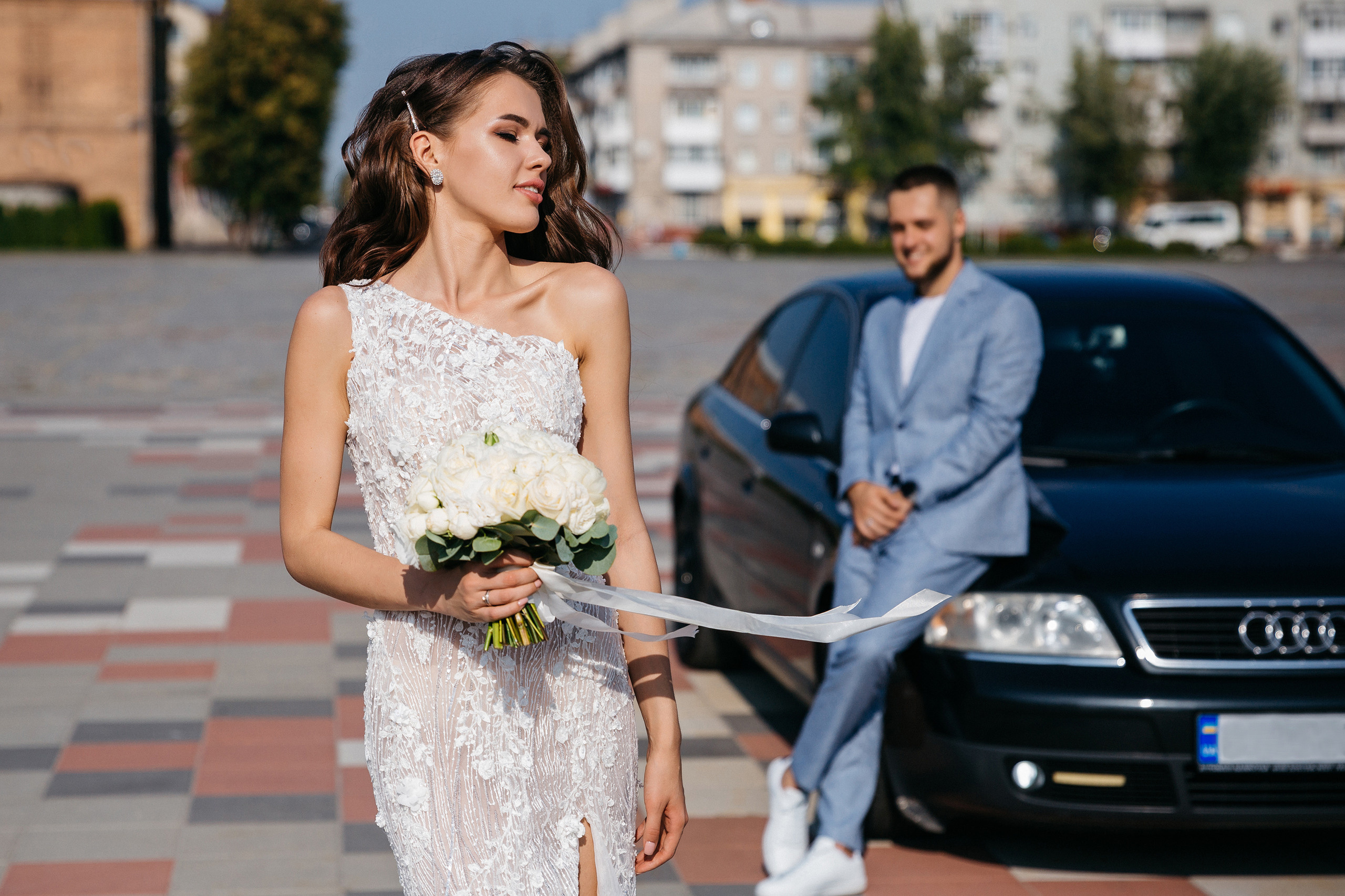Жених опирается на машину и смотрит на невесту которая идет с букетом Кременчуг