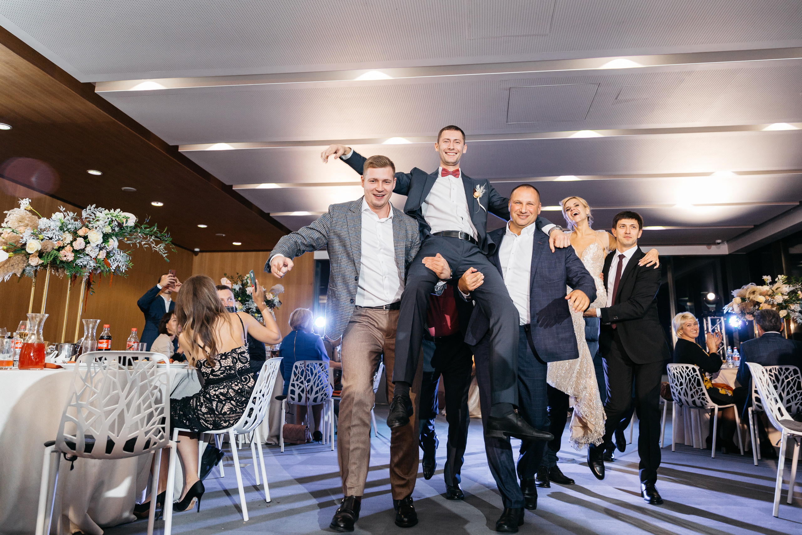 гости несут жениха во время свадебного банкета