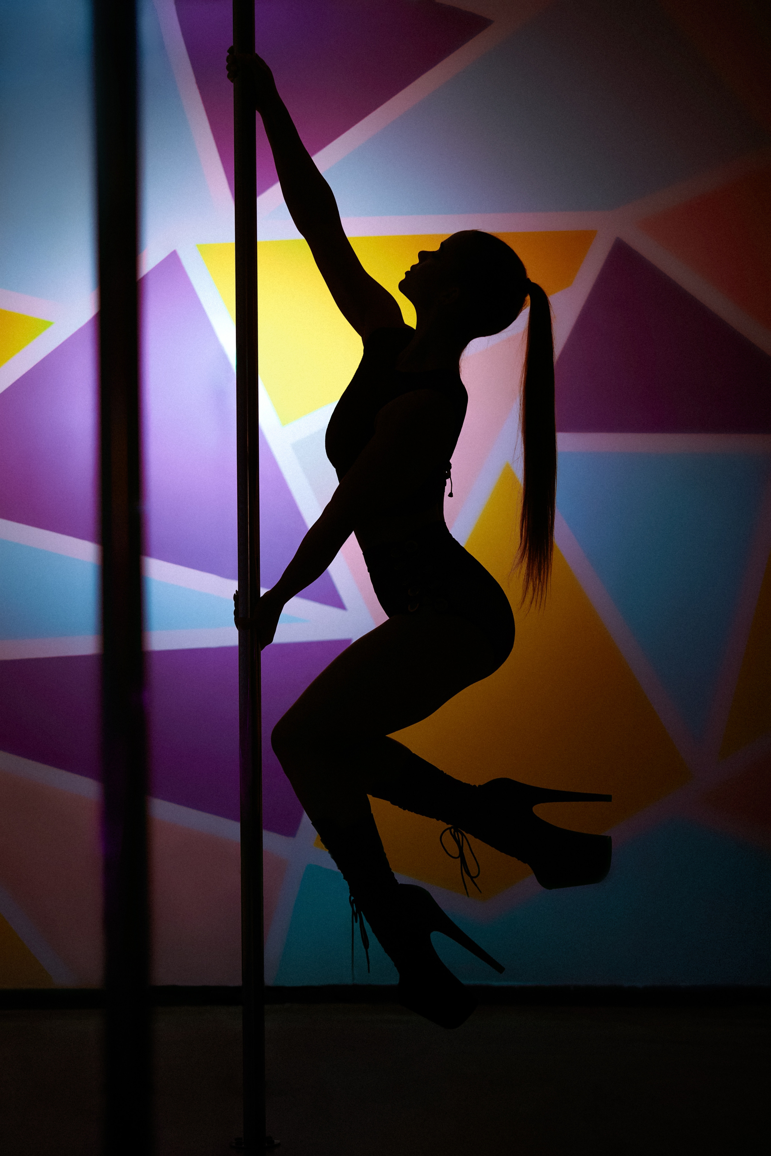 Силует танцівниці на пілоні, на фоні стіни з геометричним малюнком.