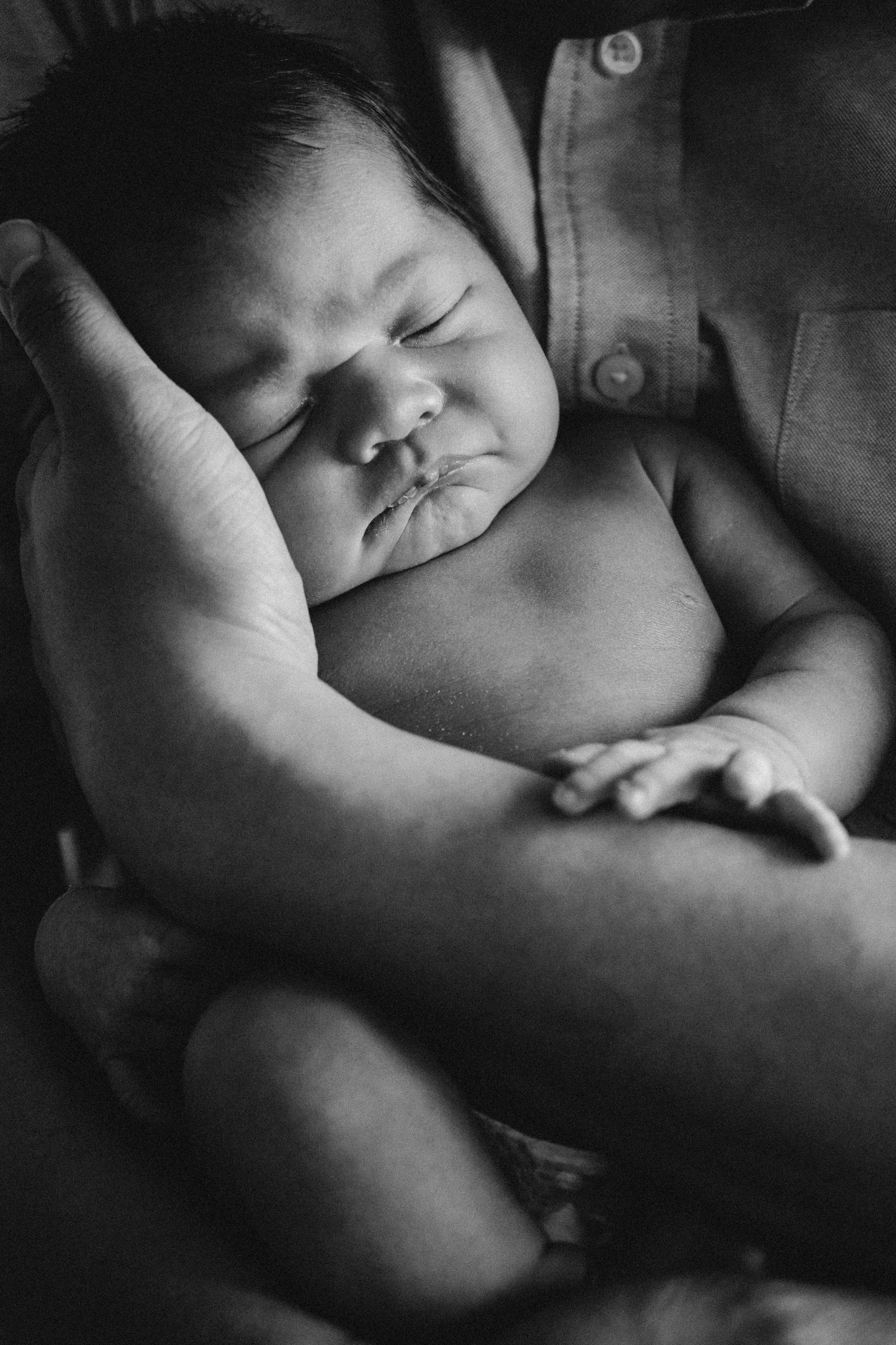 Black and white portrait of a peacefully sleeping newborn baby cradled in loving hands, newborn photography in Solihull