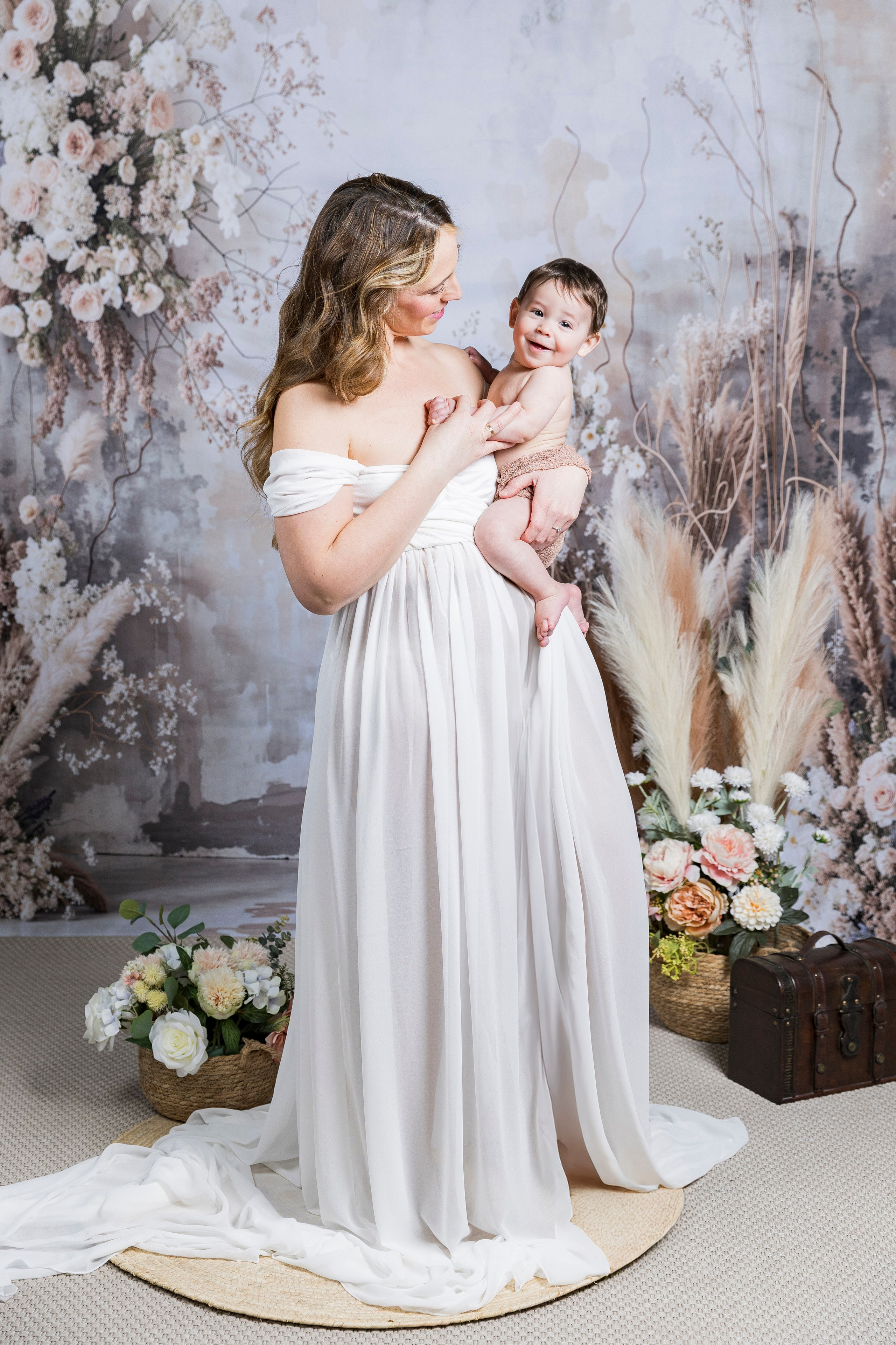 Fotografía artística de lactancia materna en estudio con decorado de flores preservadas y tonos tierra.