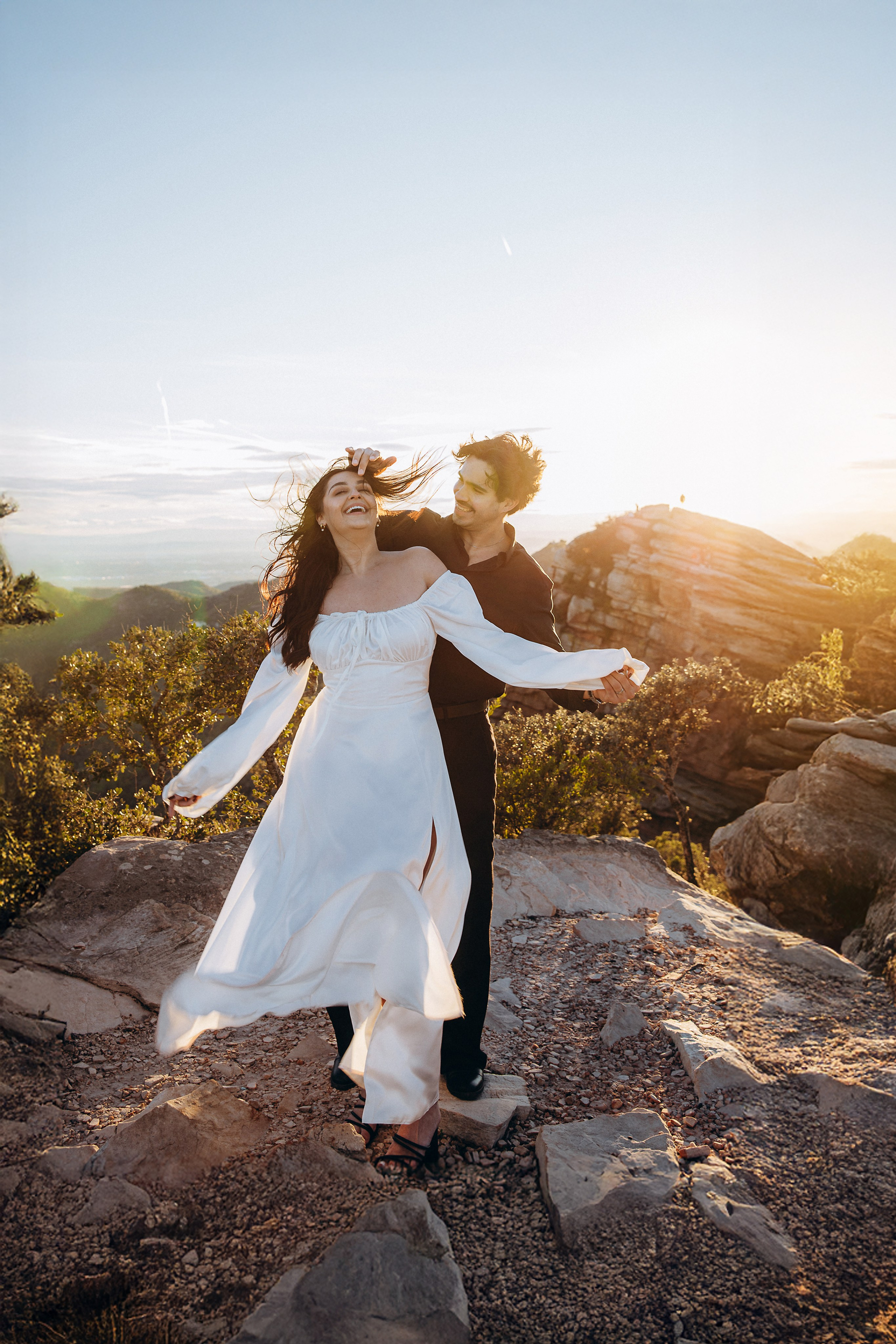 Woman in a flowing white dress turning towards her partner on a rocky mountain path near Valencia.
