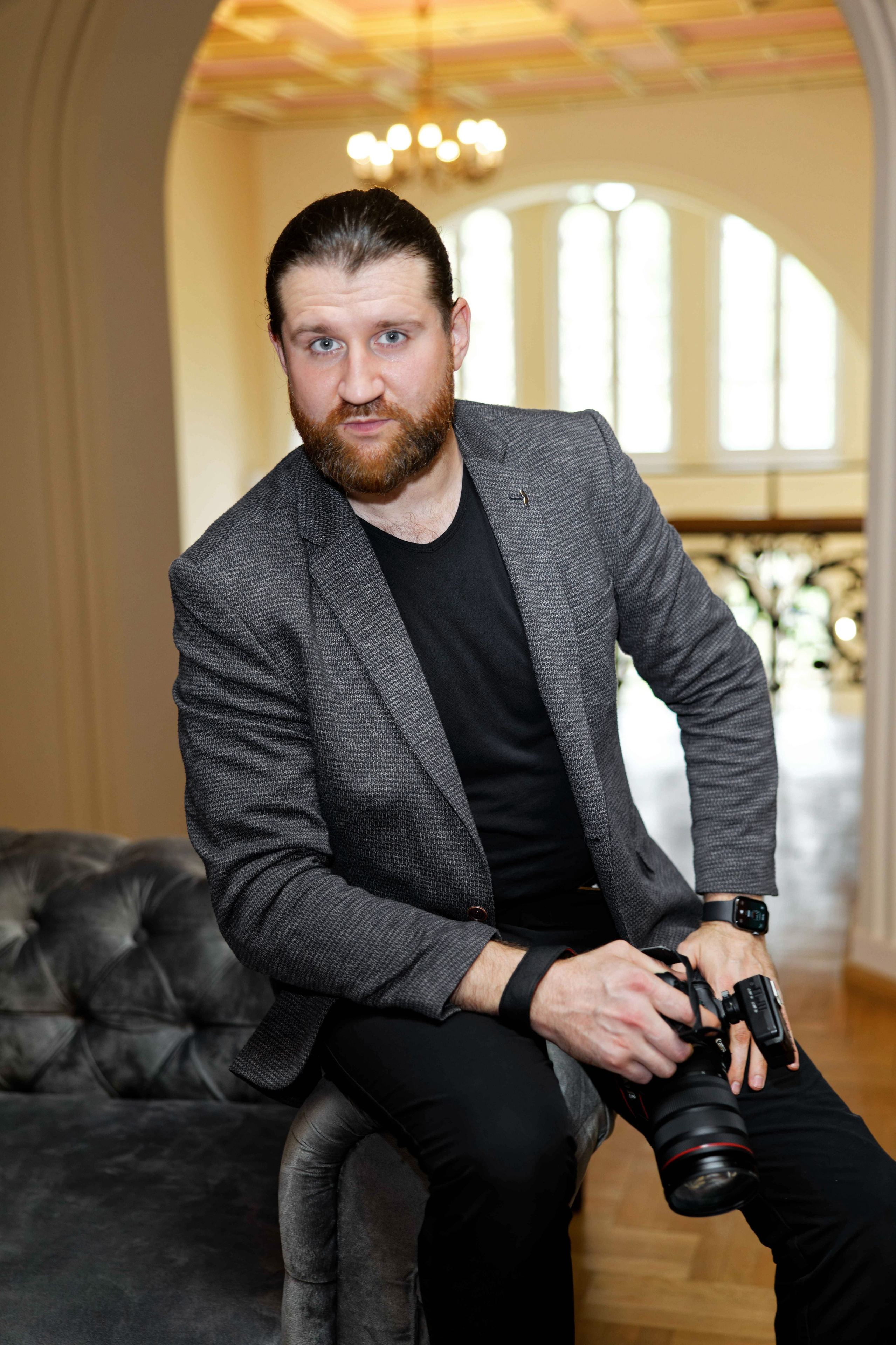 "Male wedding photographer holding a camera, wearing a dark suit."