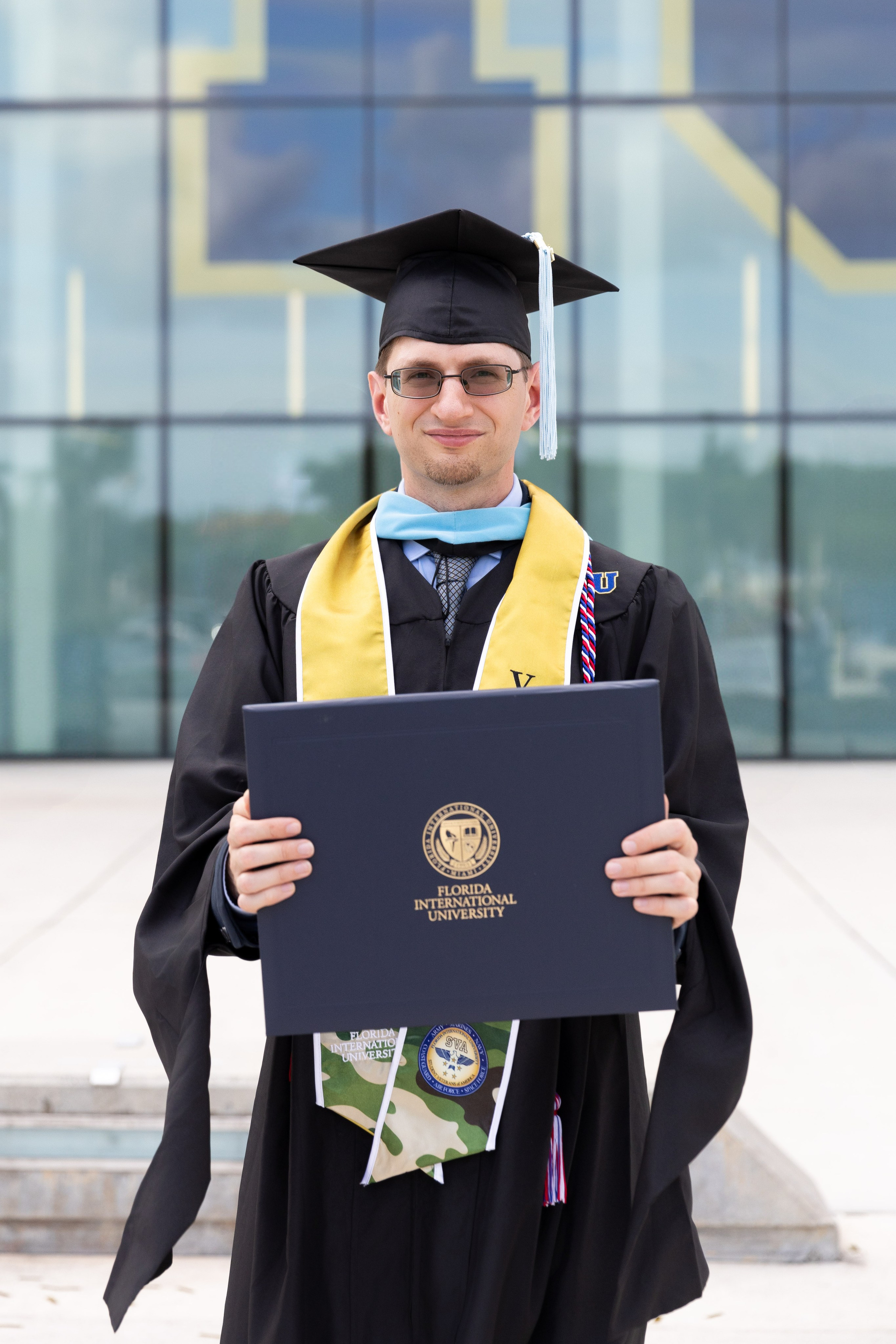 Darren holds his FIU diploma while wearing a graduation cap and gown.