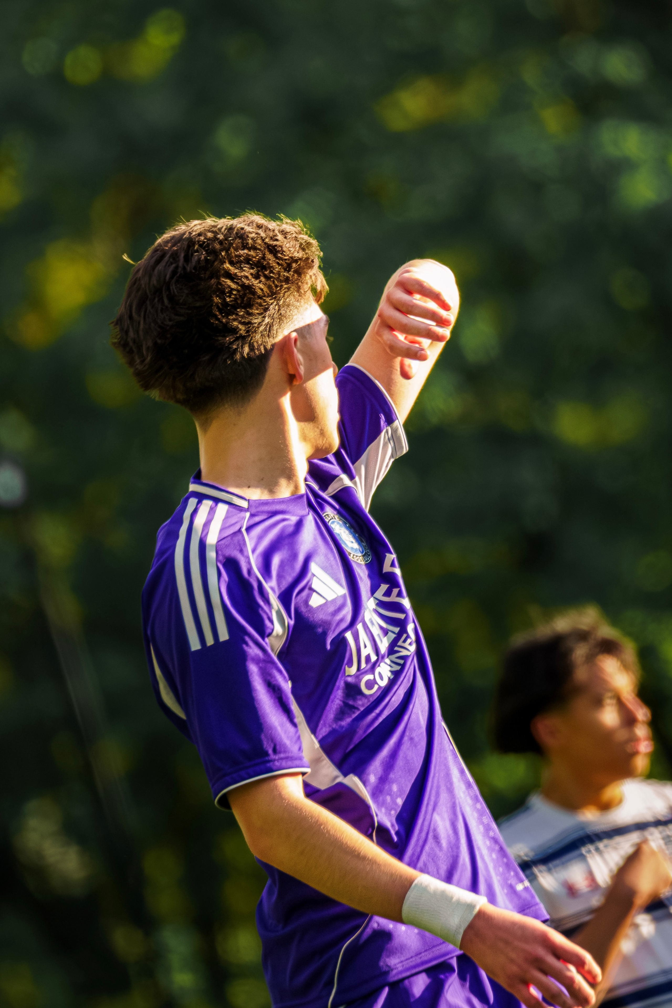 MLS Next soccer player jogging at a relaxed angle with a wide smile, captured mid-stride during a game.