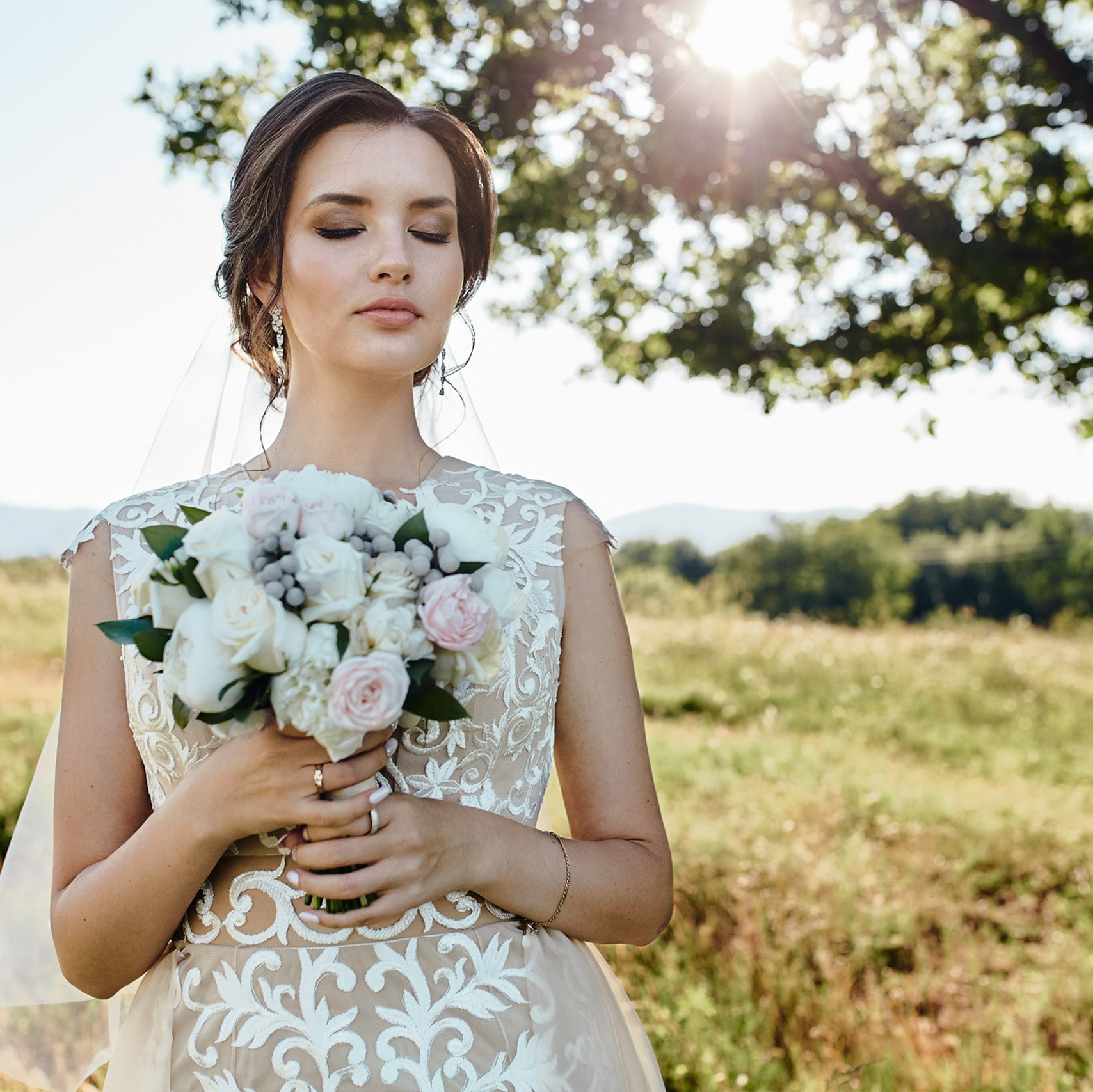 Bride holding bouquet in field, looking away