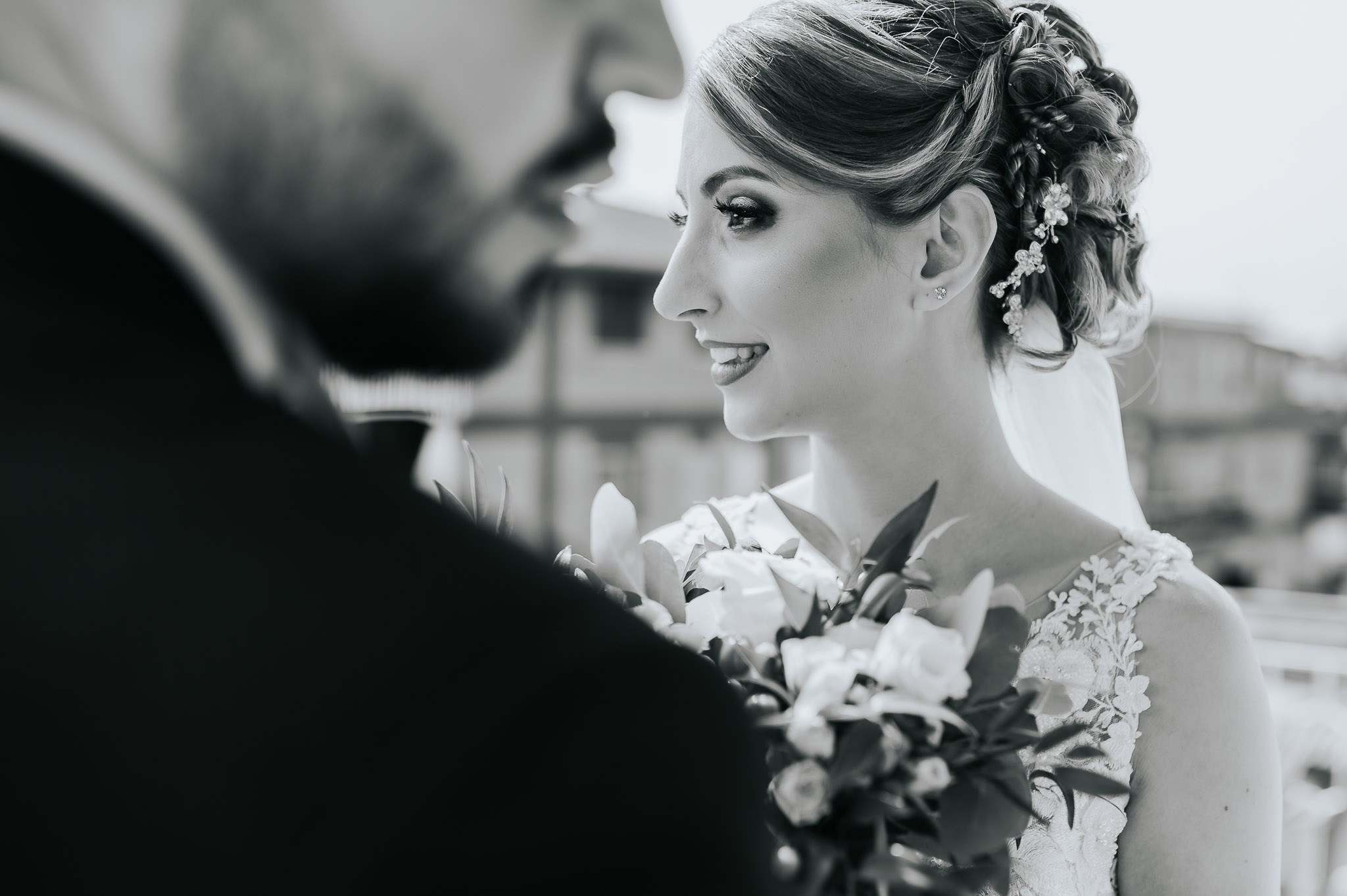 Primo piano della sposa che ammira lo sposo, con un bouquet elegante in mano e un'espressione di amore e felicità, in una fotografia in bianco e nero che cattura l'intimità del loro grande giorno.