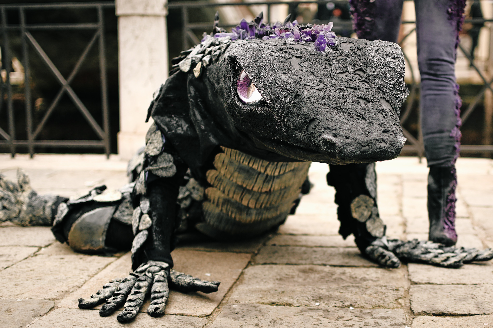 A group of performers wearing animal-inspired costumes and masks. A carnival float adorned with colorful flowers and feathers passing through a Venetian square.