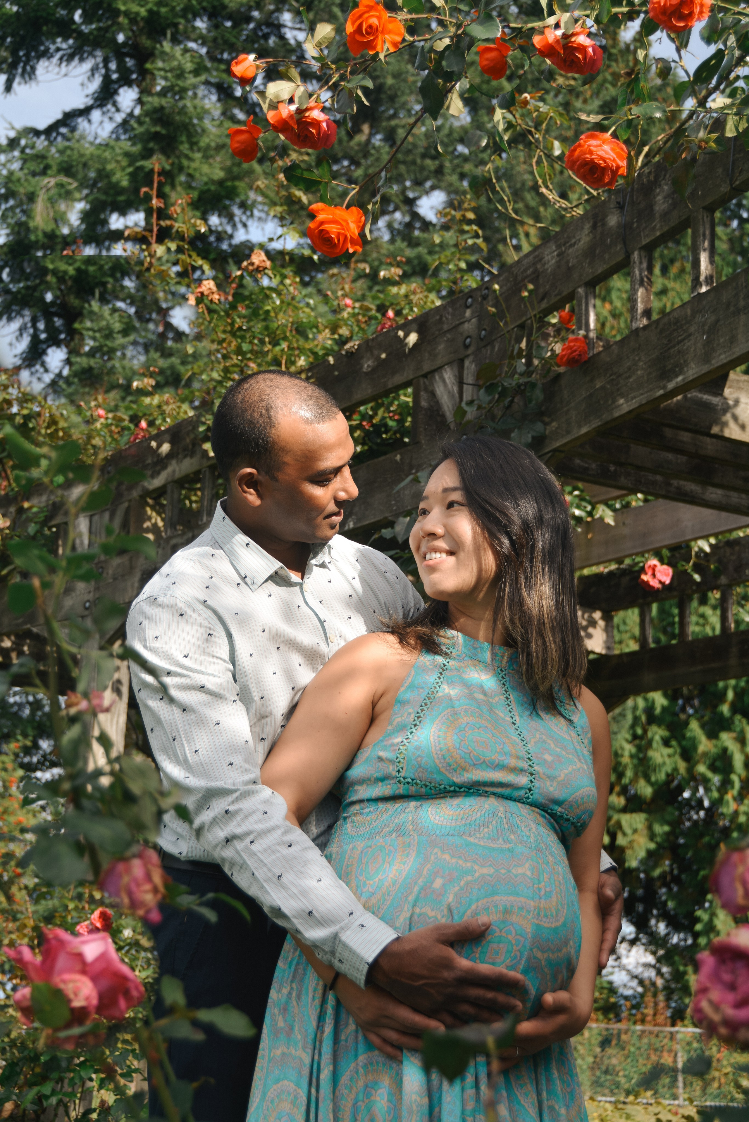 Pregnant Couple hugging in the garden among red flowers