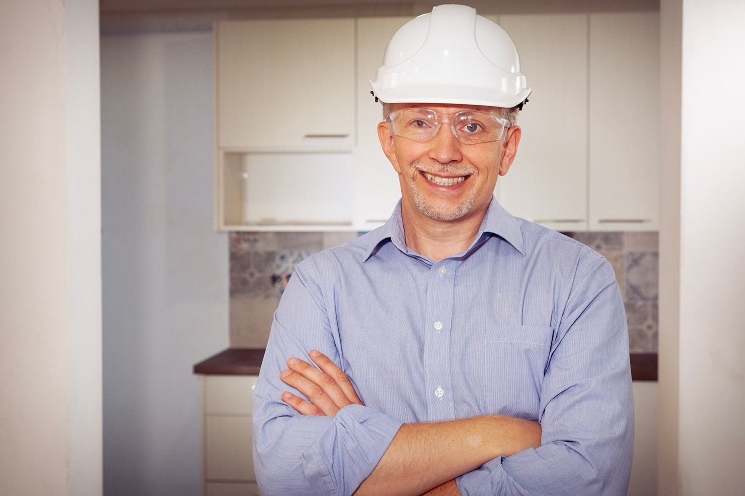 Smiling construction worker or engineer in a hard hat and safety glasses on an Athens renovation site, representing professional expertise.