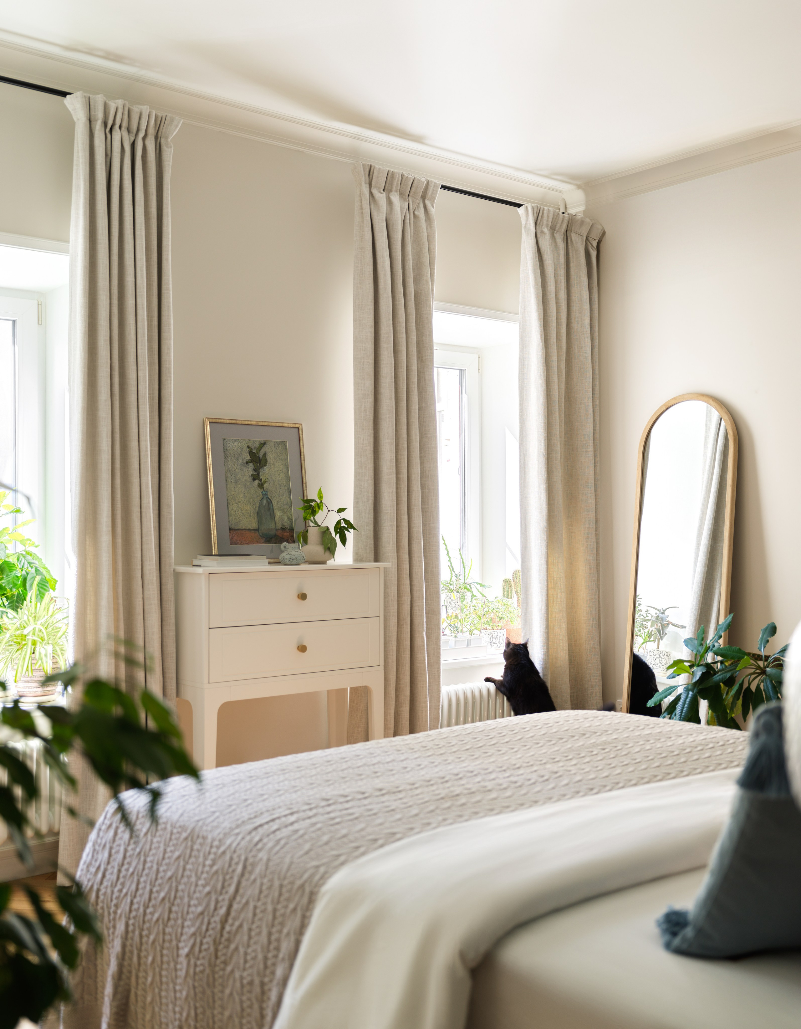 Два окна в спальне, оформленные льняными шторами.
