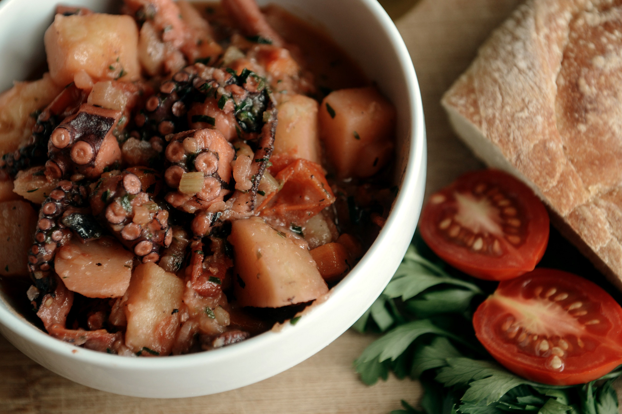 A traditional Apulian dish — stewed octopus with potatoes, carrots, and tomatoes, served in a deep bowl with bread and fresh herbs.