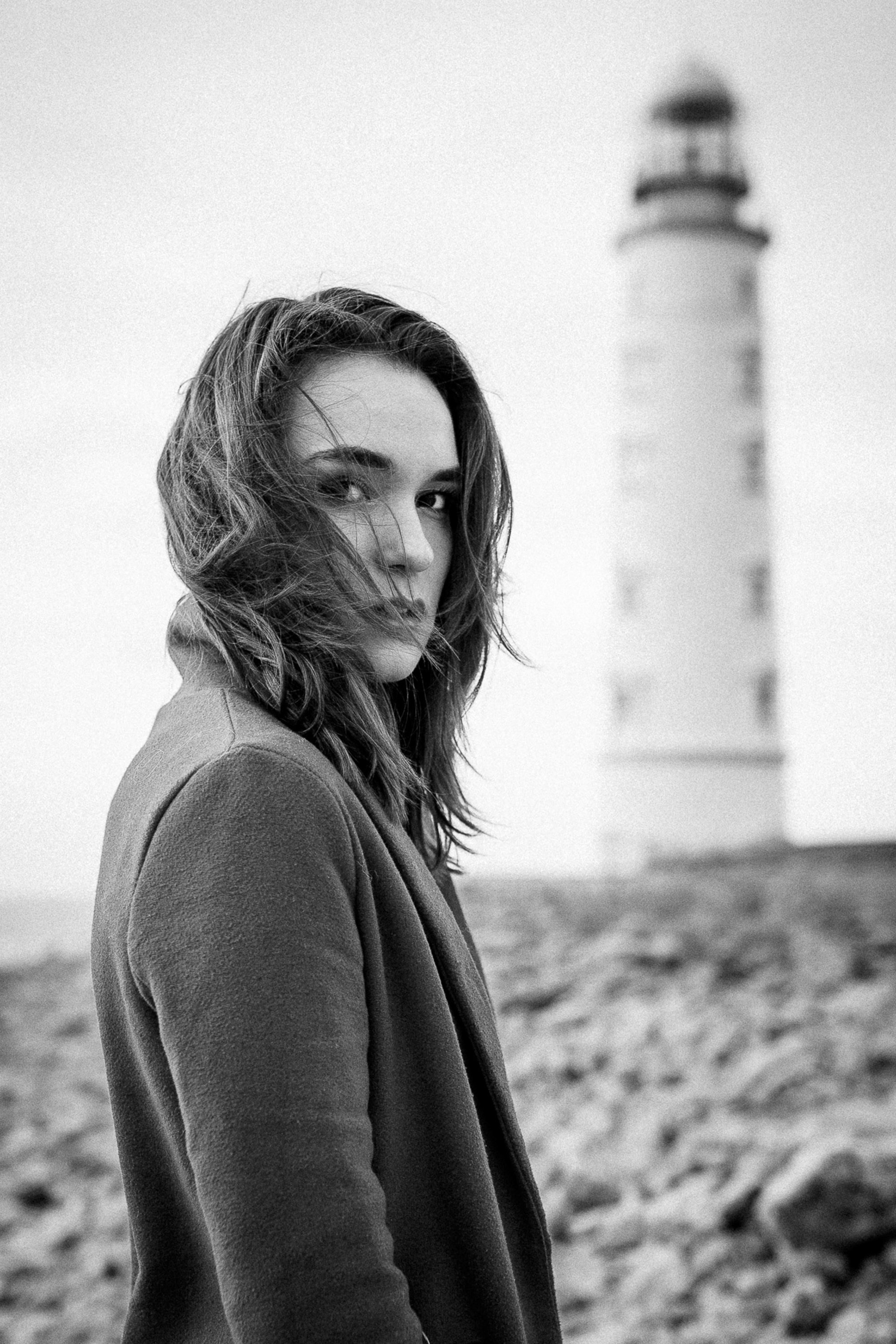 Portrait of a man with long hair standing near a lighthouse, black and white