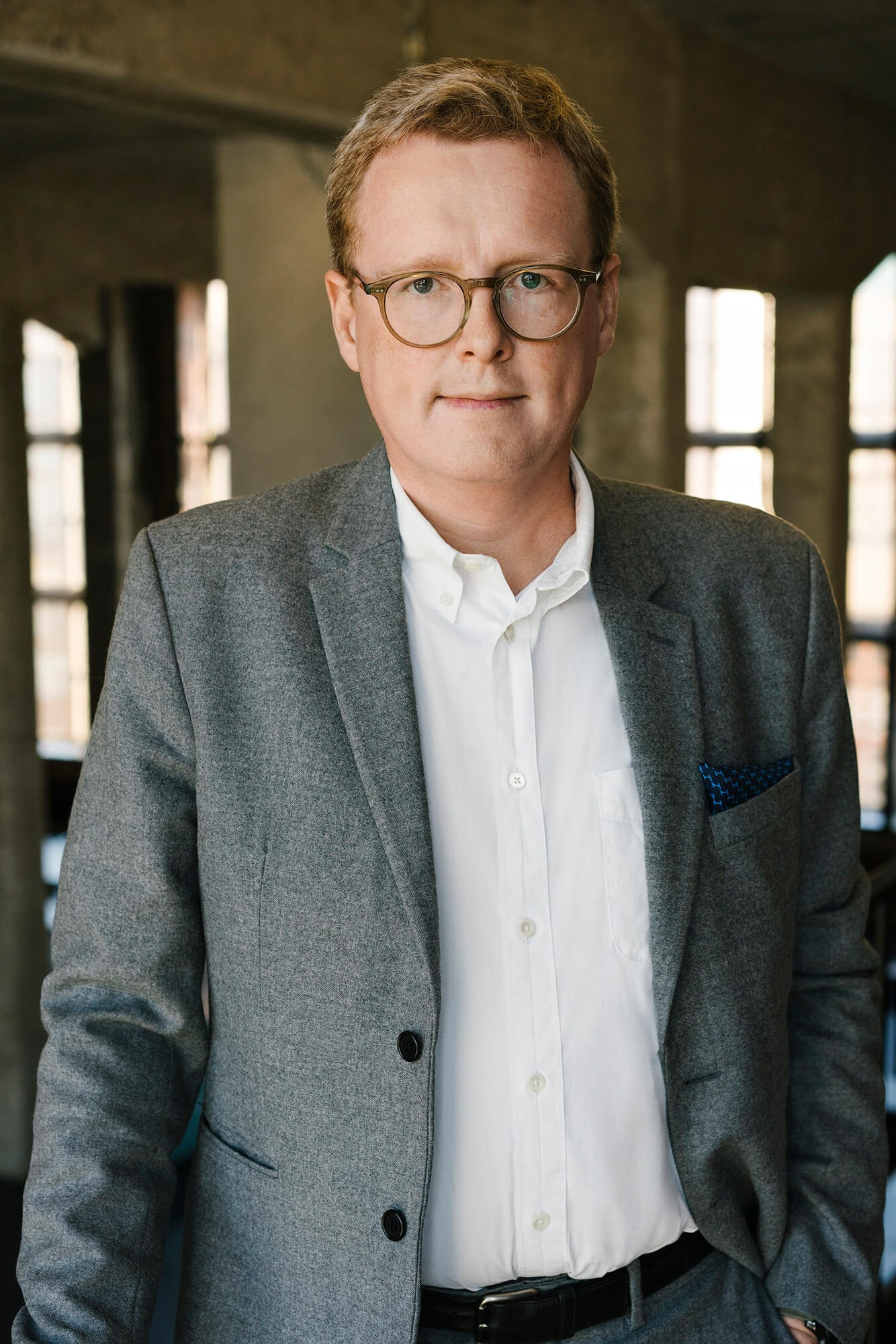 Executive-Porträt eines Mannes im grauen Blazer und mit Brille im modernen Büro (professionelles Corporate-Headshot bei natürlichem Licht)
