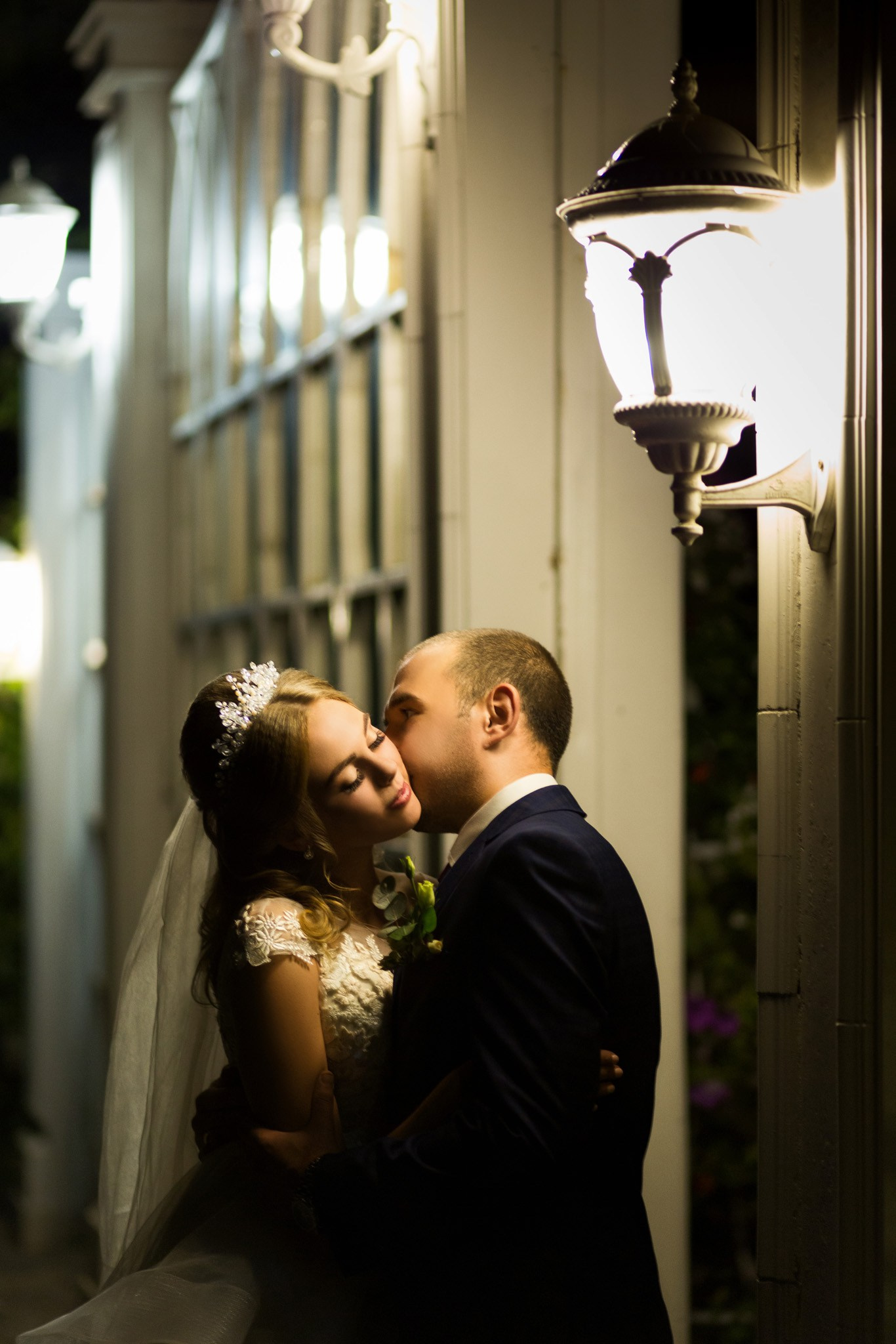 пара молодят стоять біля вуличного світильника, який розташований на стіні