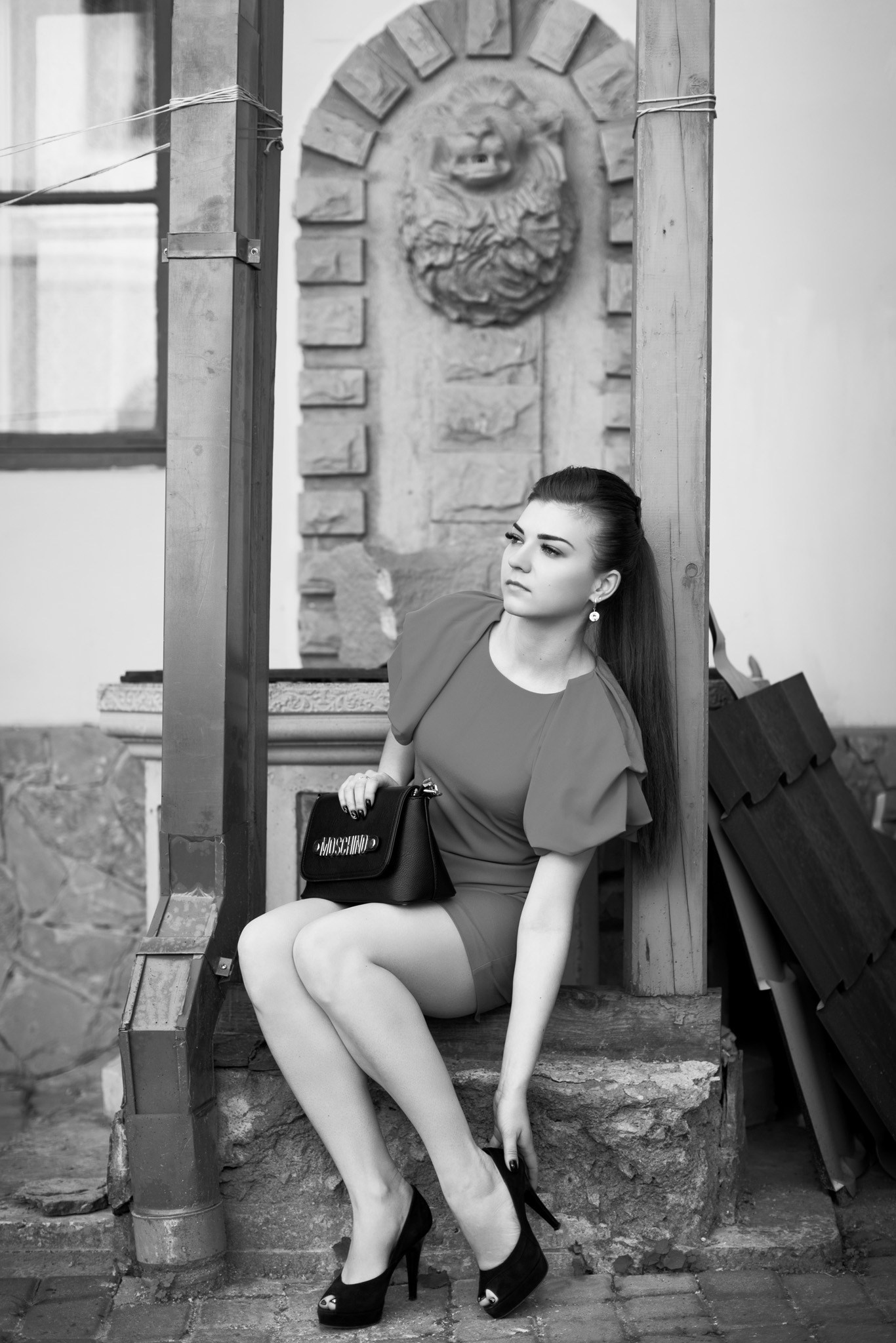 на фотографії дівчина сидить на бордюрі і поправляє туфельку