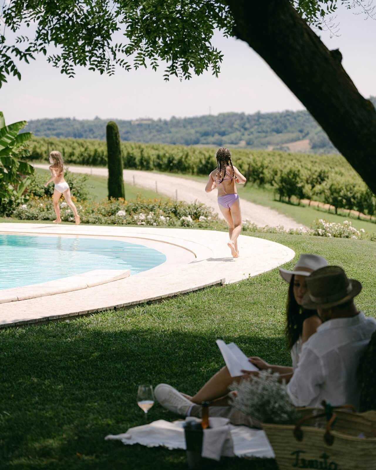 Guests relaxing by a hillside villa pool overlooking the vineyards of the Langhe in August