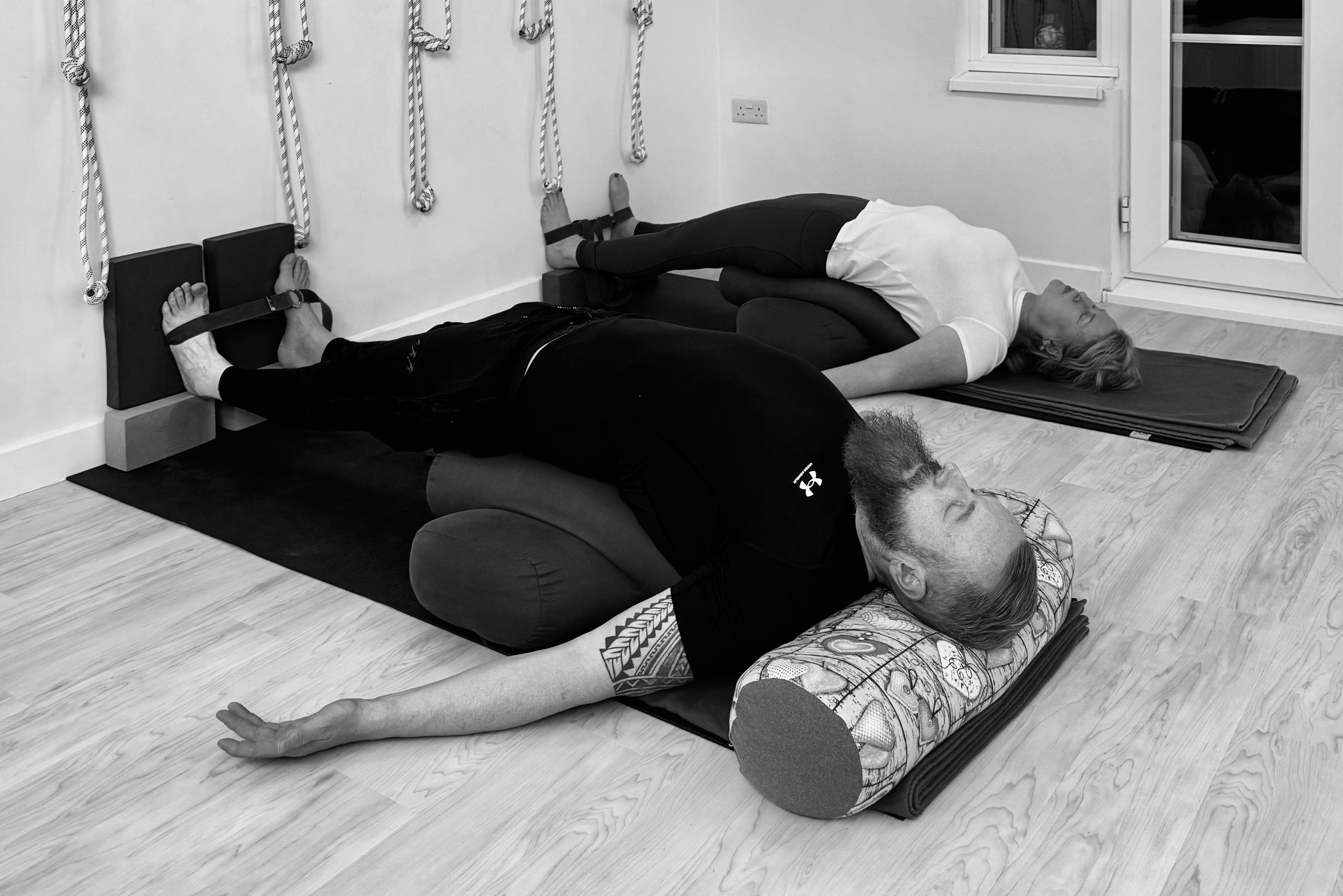 Couple in supported restorative Iyengar yoga pose using bolsters and wall ropes in Solihull studio.