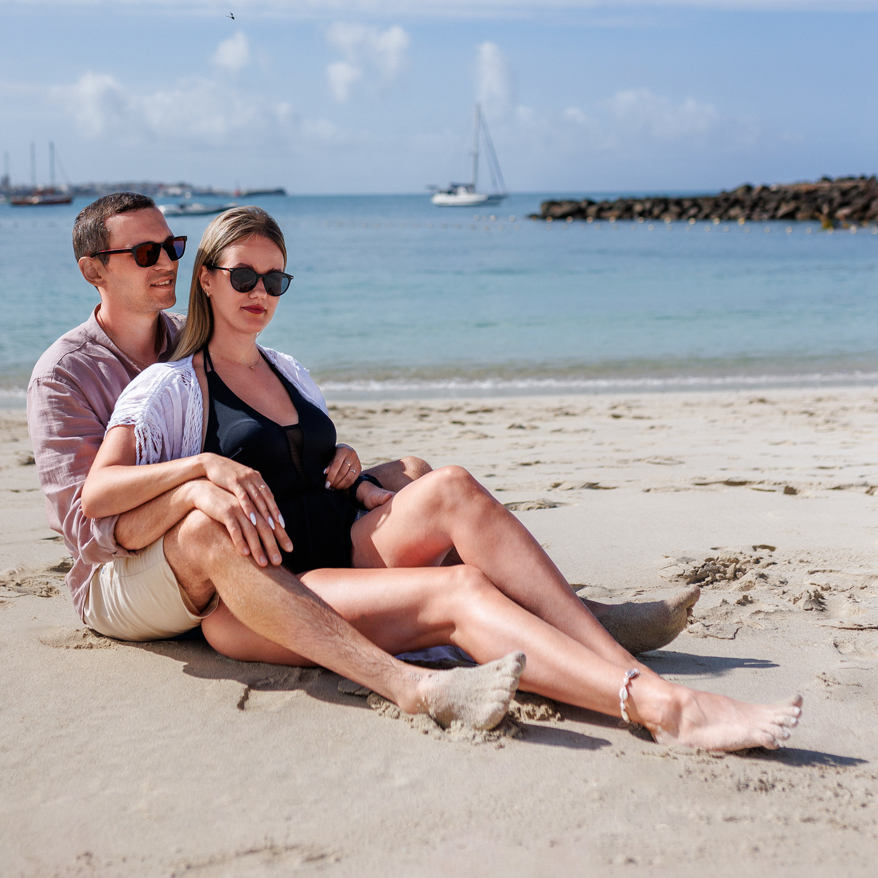 Anfi del Mar is a professional photographer in Gran Canaria A couple sits on the beach with a boat in the background.