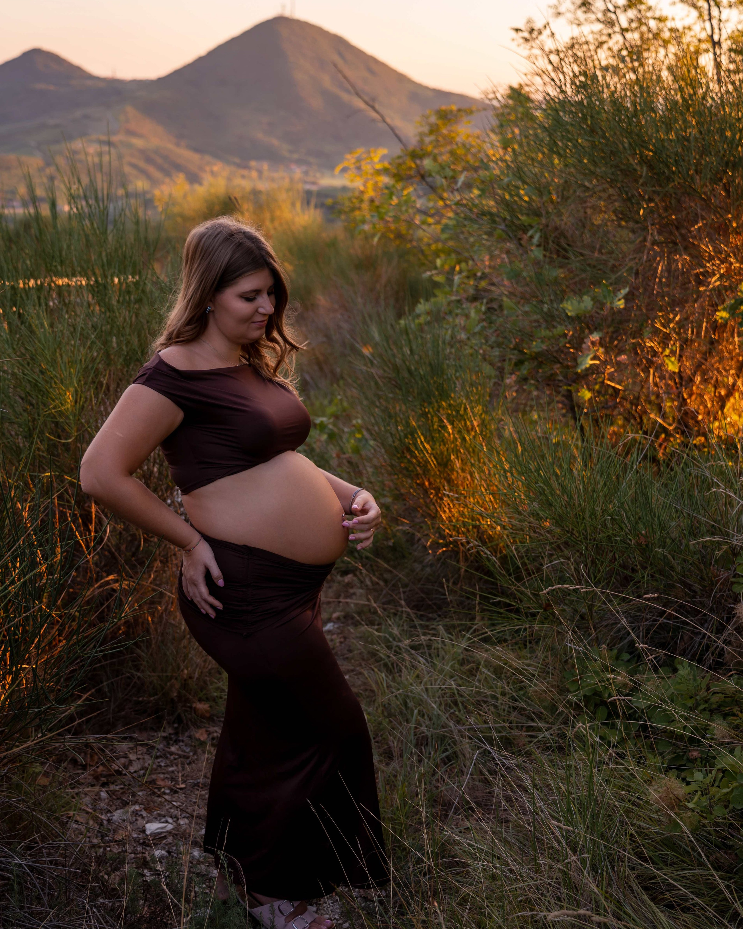 Ritratto di una futura mamma in abito scuro immersa nella natura durante una sessione fotografica gravidanza all'aperto.