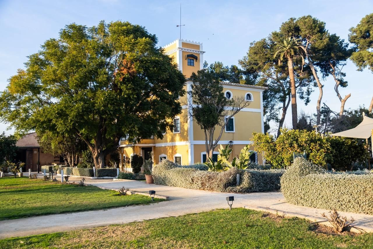 Yellow villa and tower surrounded by mature trees, lawns and garden paths at La Huerta by Bonho wedding venue.
