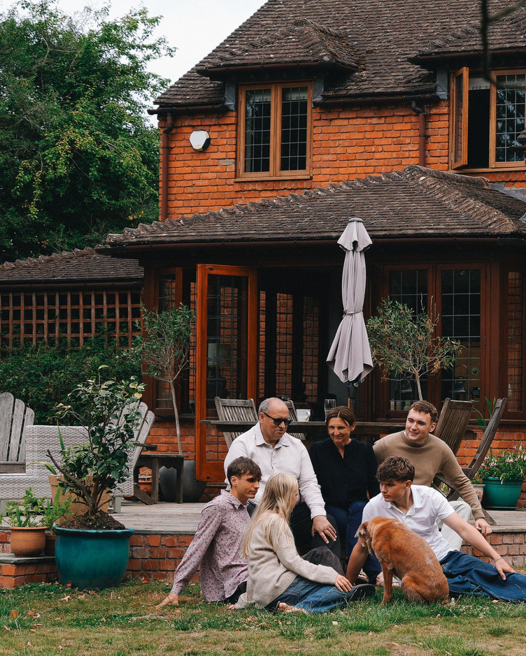 Family sitting together on the grass outside a countryside house during a natural outdoor family photo session