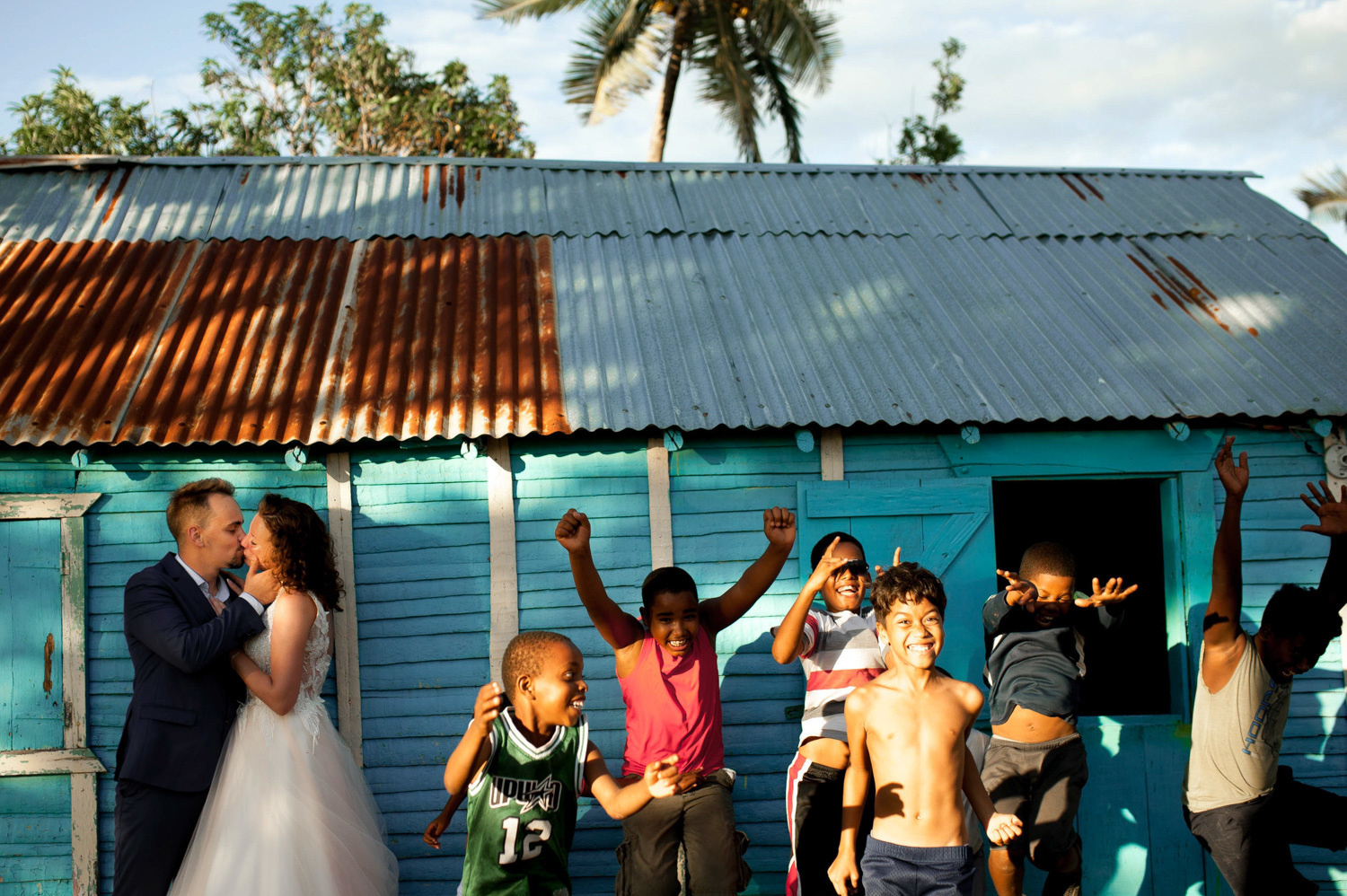 The newlyweds are kissing in front of the Dominican Cabin, and the children are bouncing up at this point.