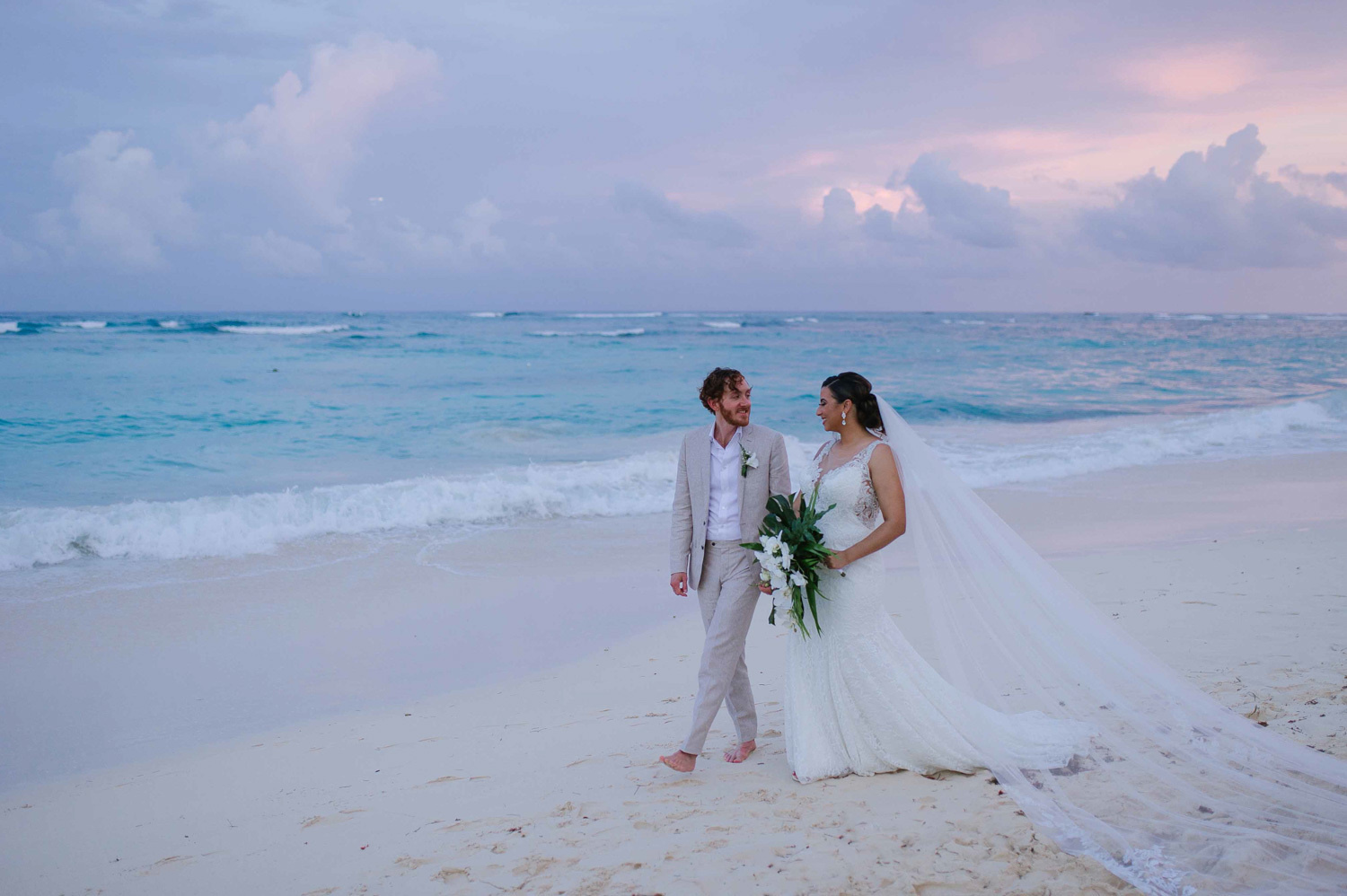 The bride and groom hold hands during a photo shoot along the shoreline. 