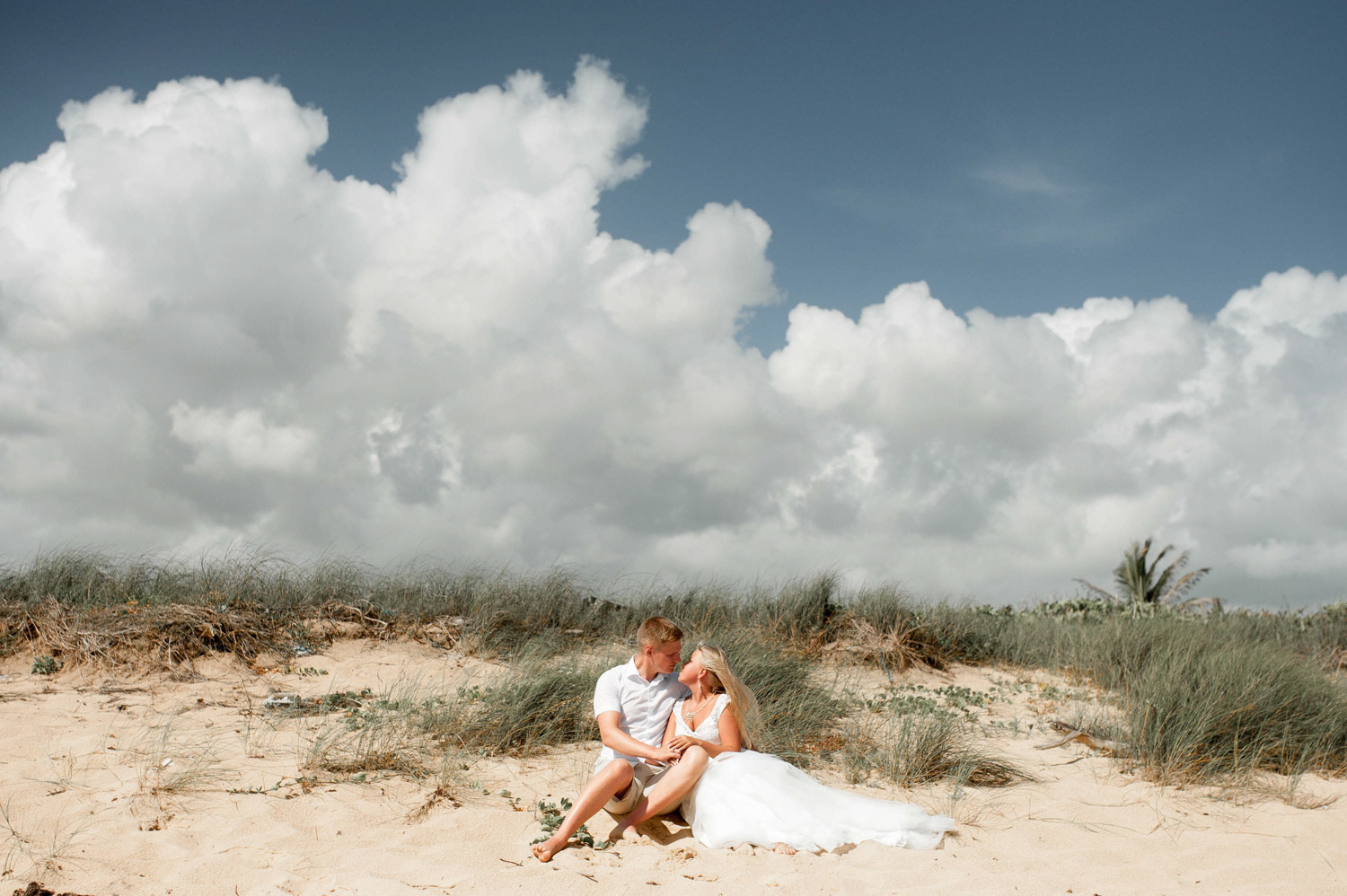 The bride and groom hold each other's hands in a photo shoot against a backdrop of giant clouds.