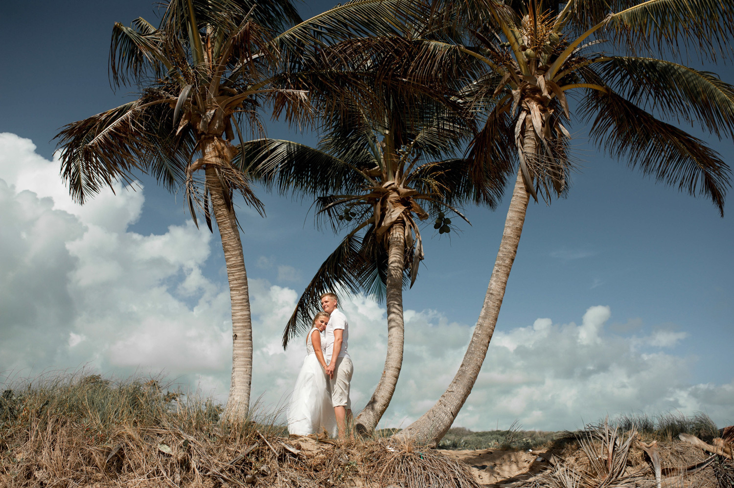 A couple posing for a photo between the palm trees.