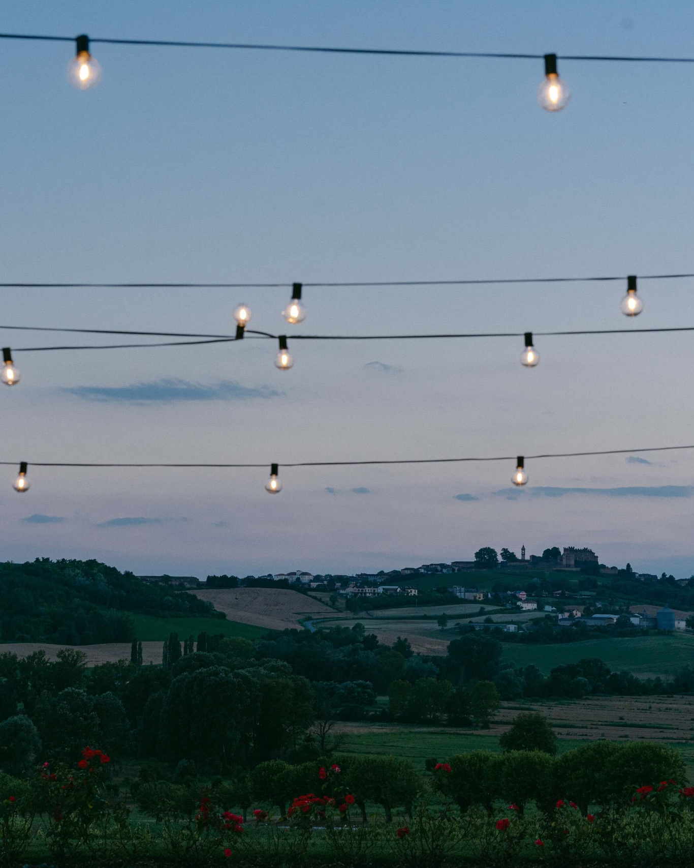 Evening view over the hills and vineyards of Piedmont with string lights above a wedding villa garden