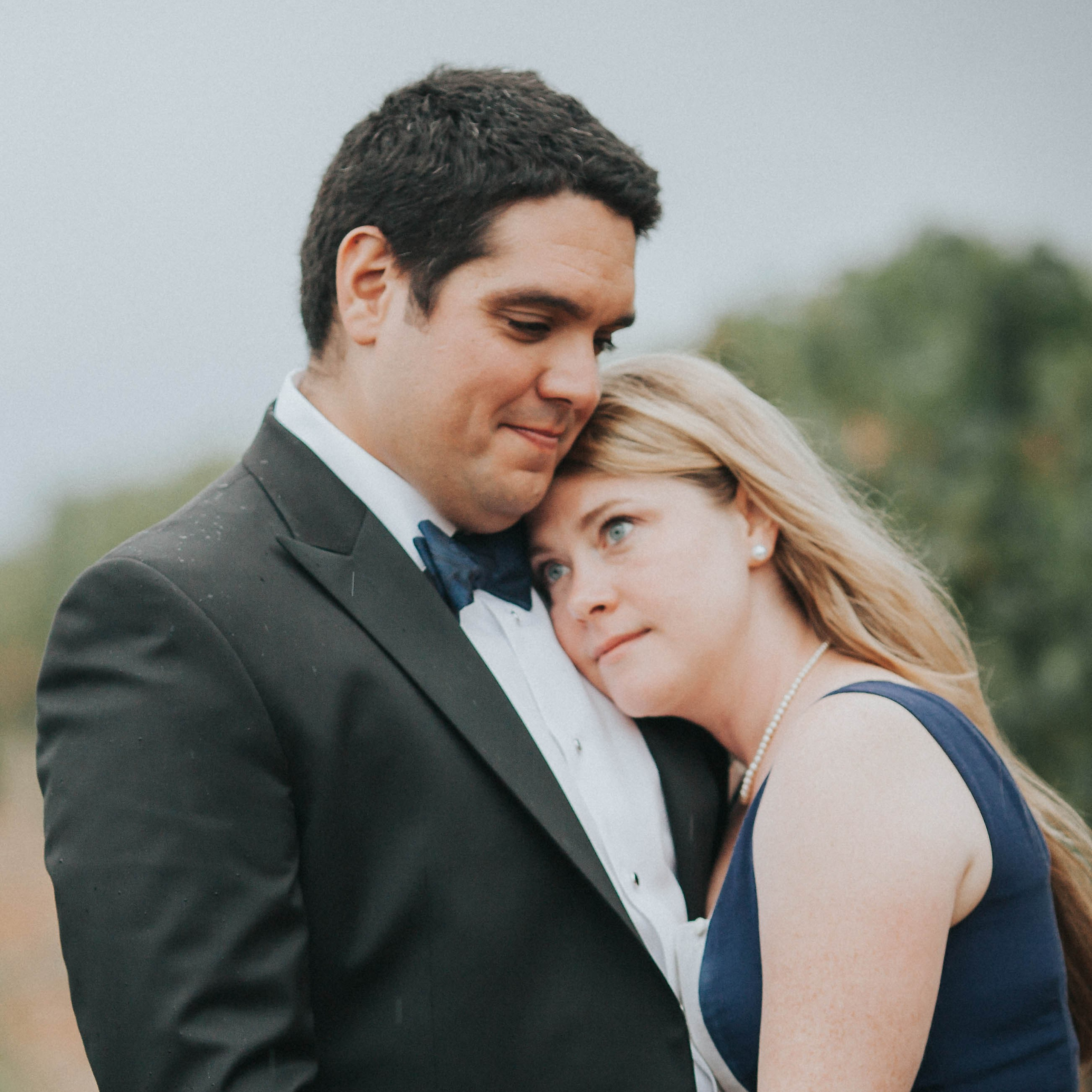 Red-haired bride holding her flowing veil aloft smiles seductively to her bouquet holding groom as he leans back against a railing in appreciation at the Vrtba Garden in Prague. 