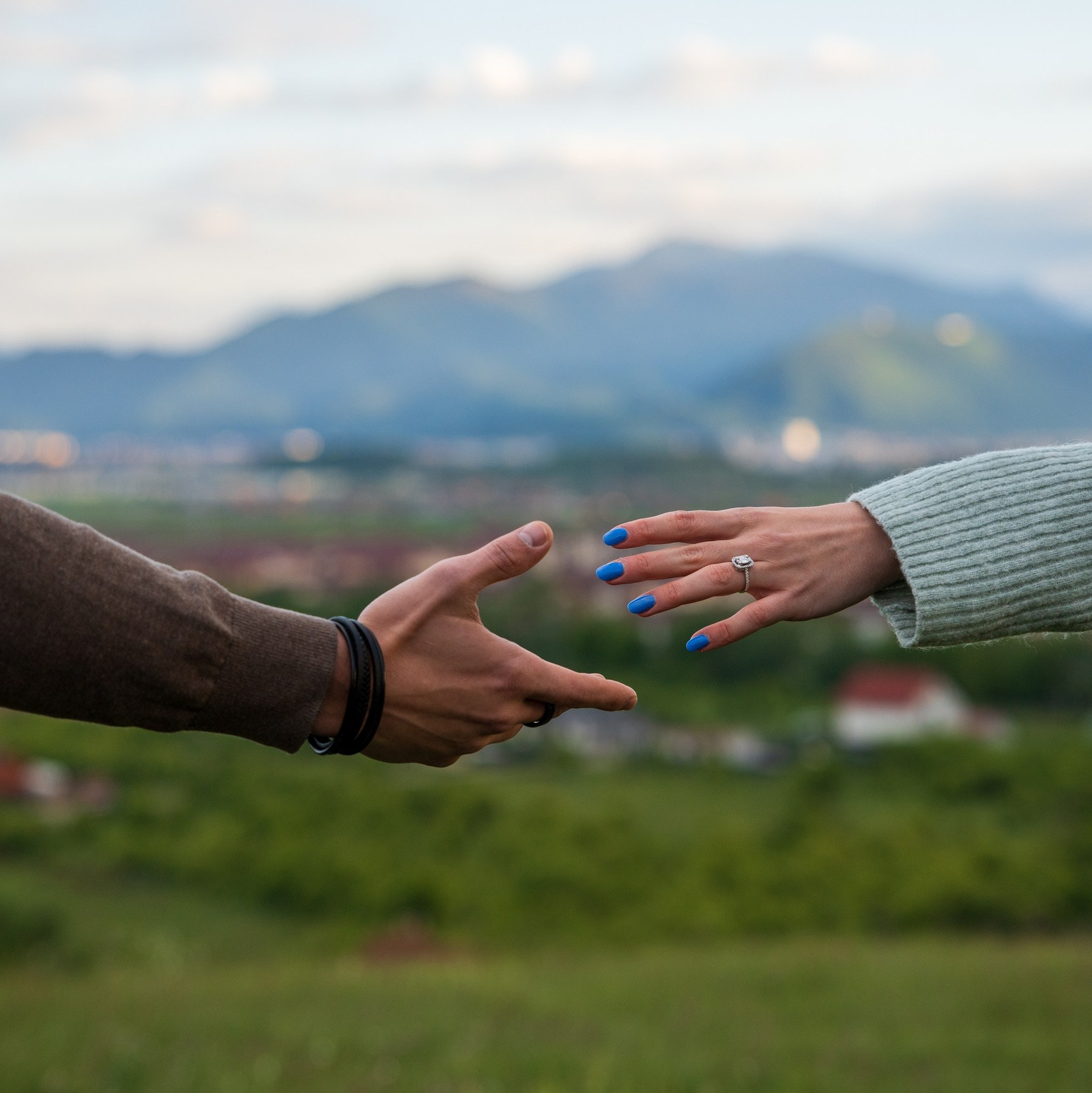 A couple reaching for each other’s hands with mountains in the background