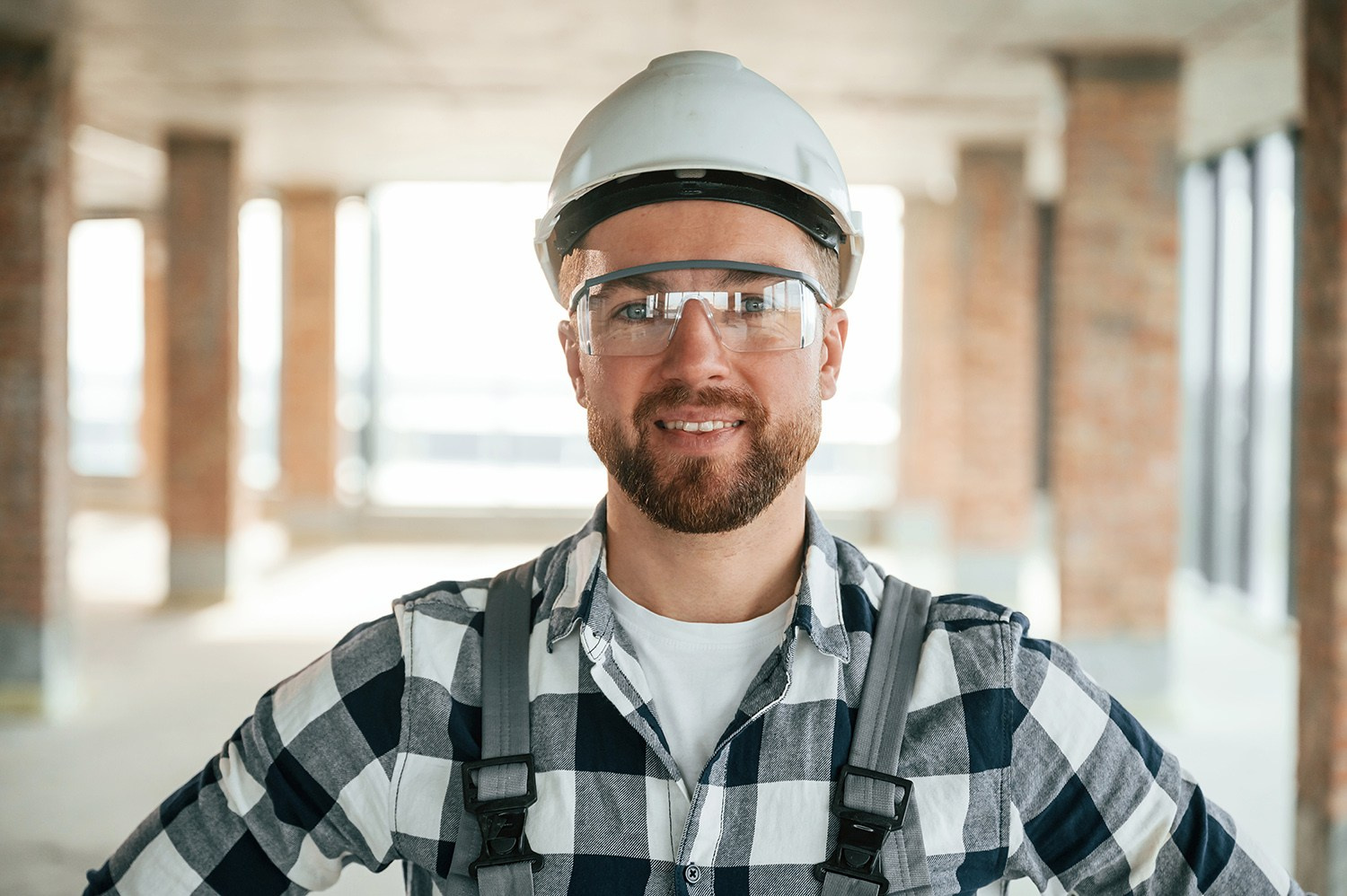 Smiling construction worker or engineer in a hard hat and safety glasses on an Athens renovation site, representing professional expertise.