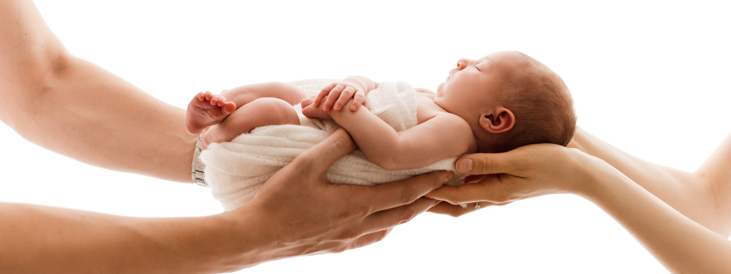 Delikatna sesja noworodkowa. Maluszek trzymany w dłoniach rodziców.