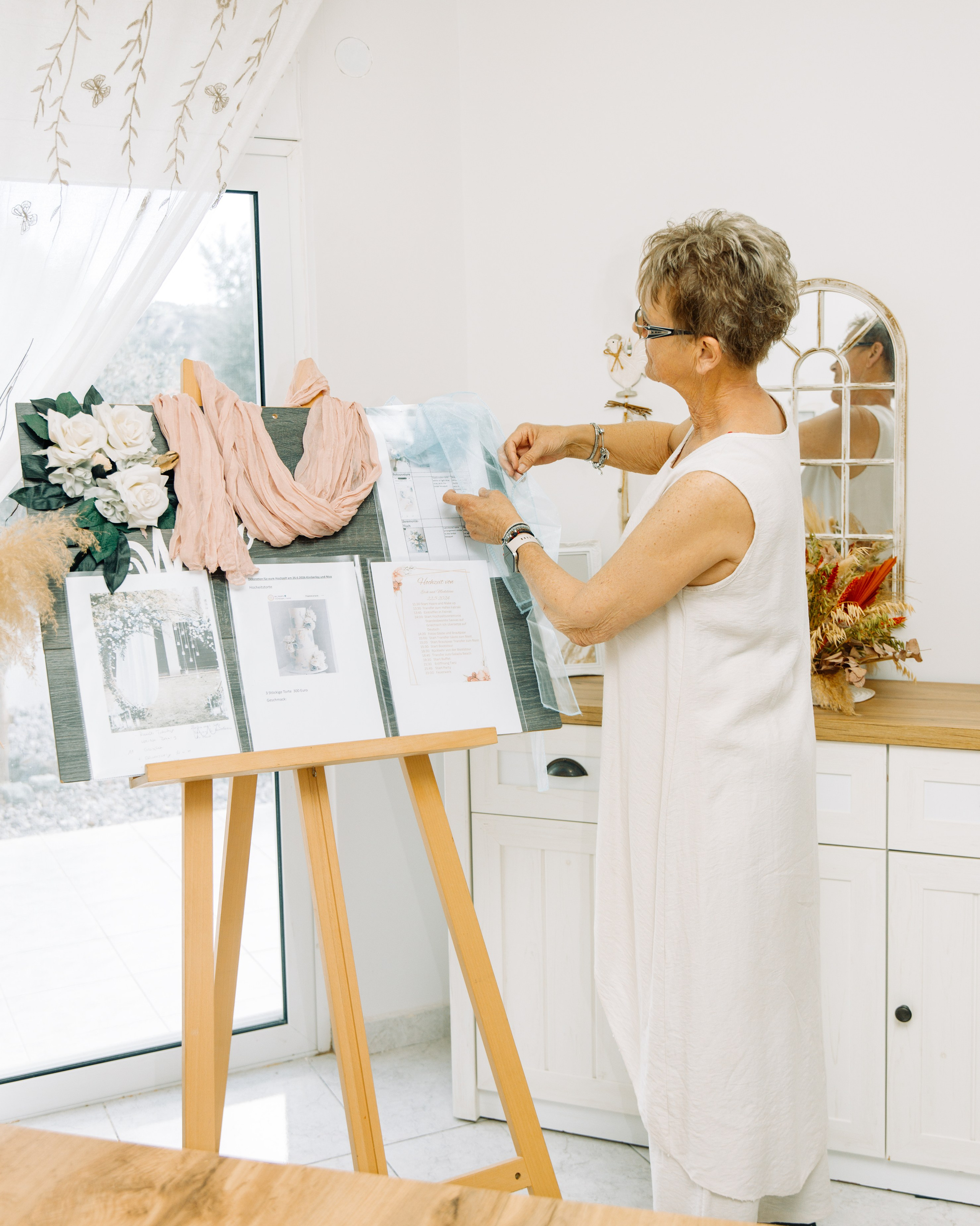 Wedding designer Renate Woeste in Rhodes arranging artificial flowers and a pink drape on a creative presentation board, showcasing wedding inspiration for Lindos and Kalithea venues.