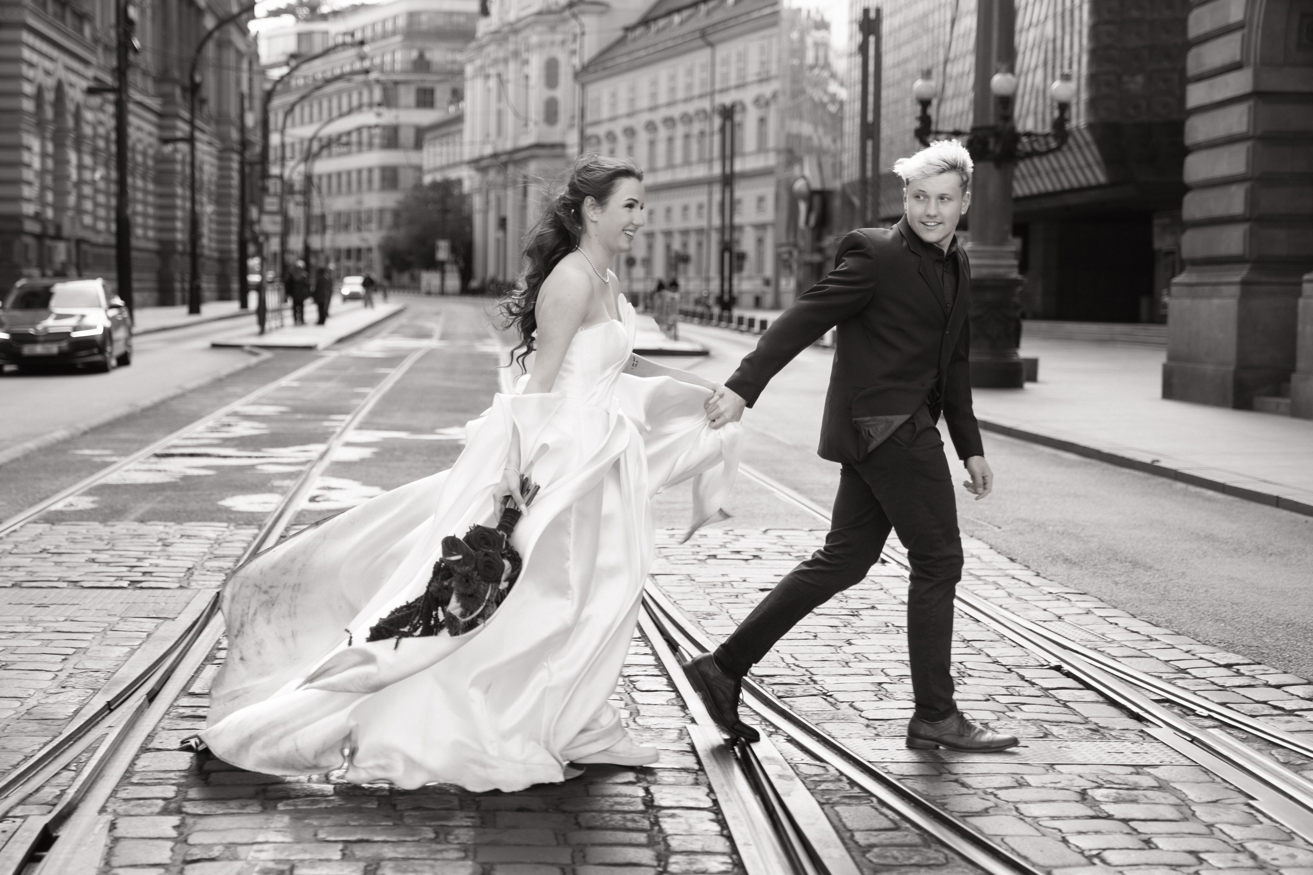 Elopement v Praze, nevěsta a ženich přecházejí ulici v historickém centru.