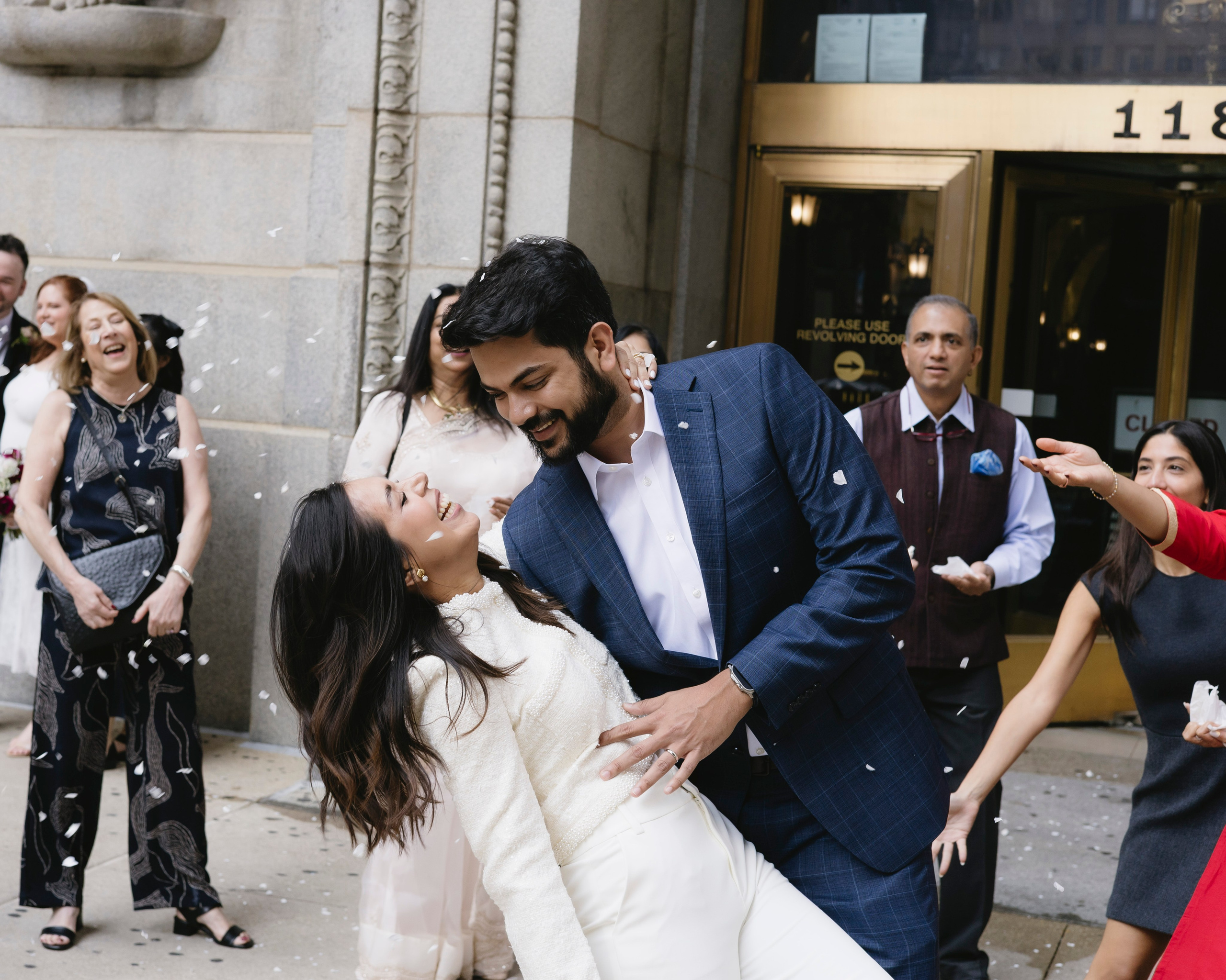 Couple about to kiss at the Chicago City Hall entrance while guests laugh and celebrate around them.