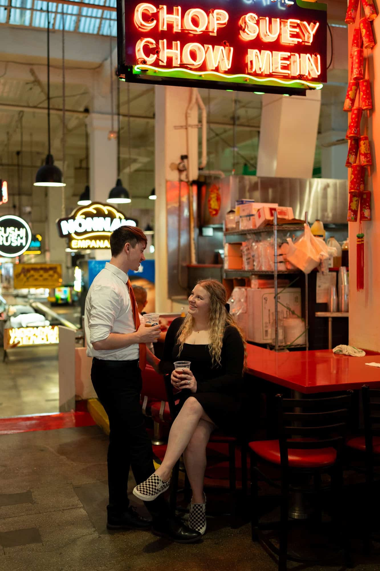 Candid engagement photo of couple sharing drinks and laughing at Grand Central Market Los Angeles