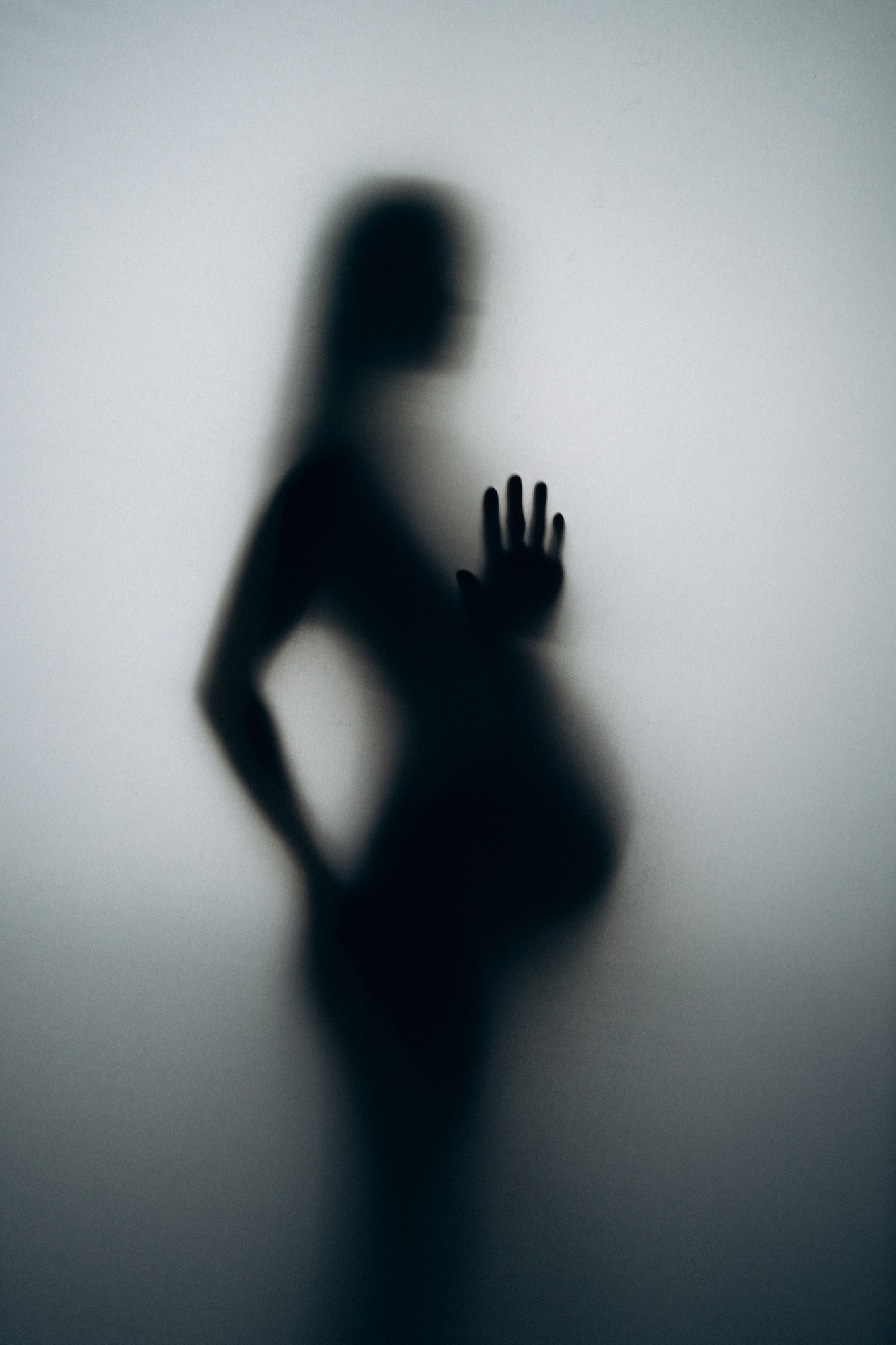 Художественный силуэт беременной женщины за матовым стеклом — креативная съемка беременности