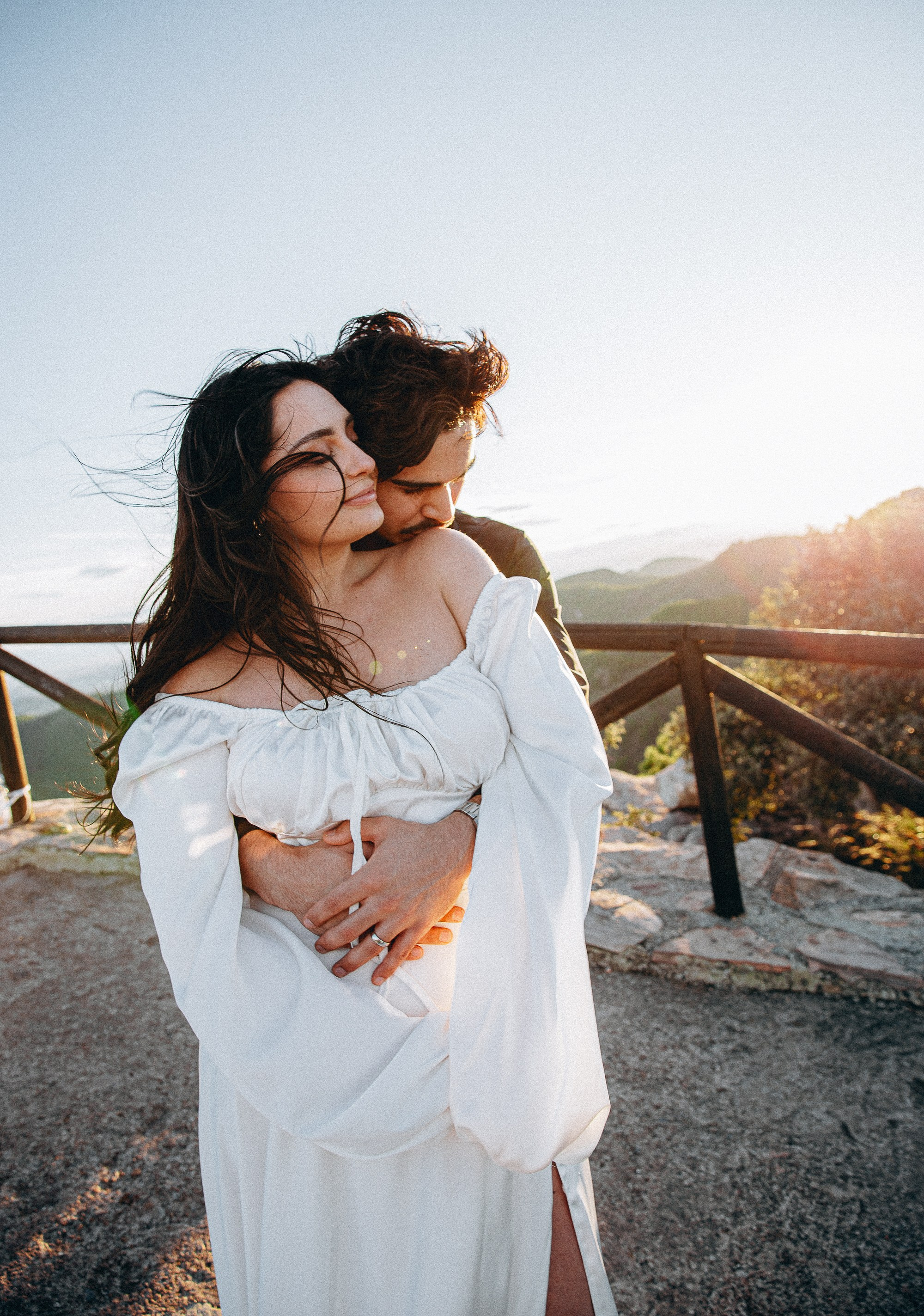 Man embracing his smiling partner from behind at a mountain viewpoint near Valencia in evening light.