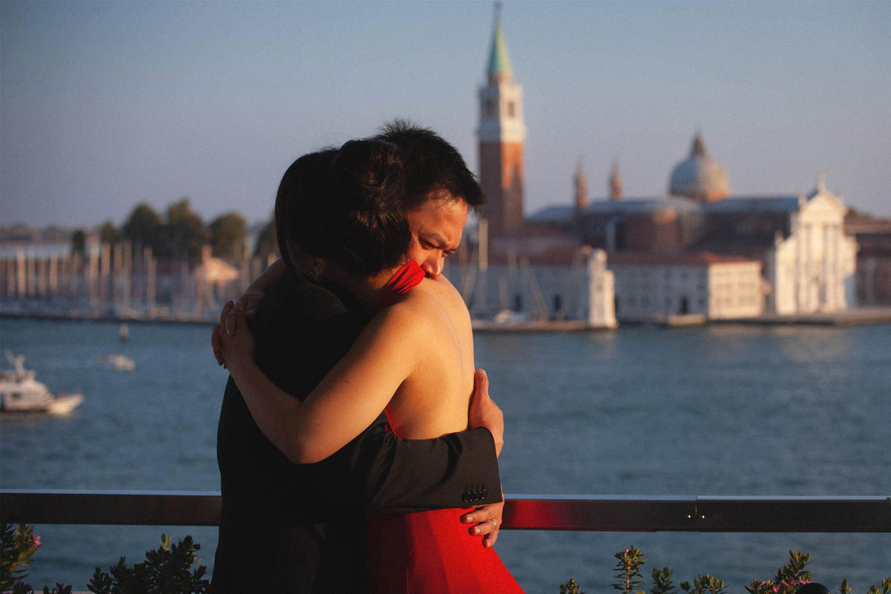 A Thai couple shares an emotional embrace at the rooftop terrace of the Hotel Danieli overlooking the canals of Venice at sunset.