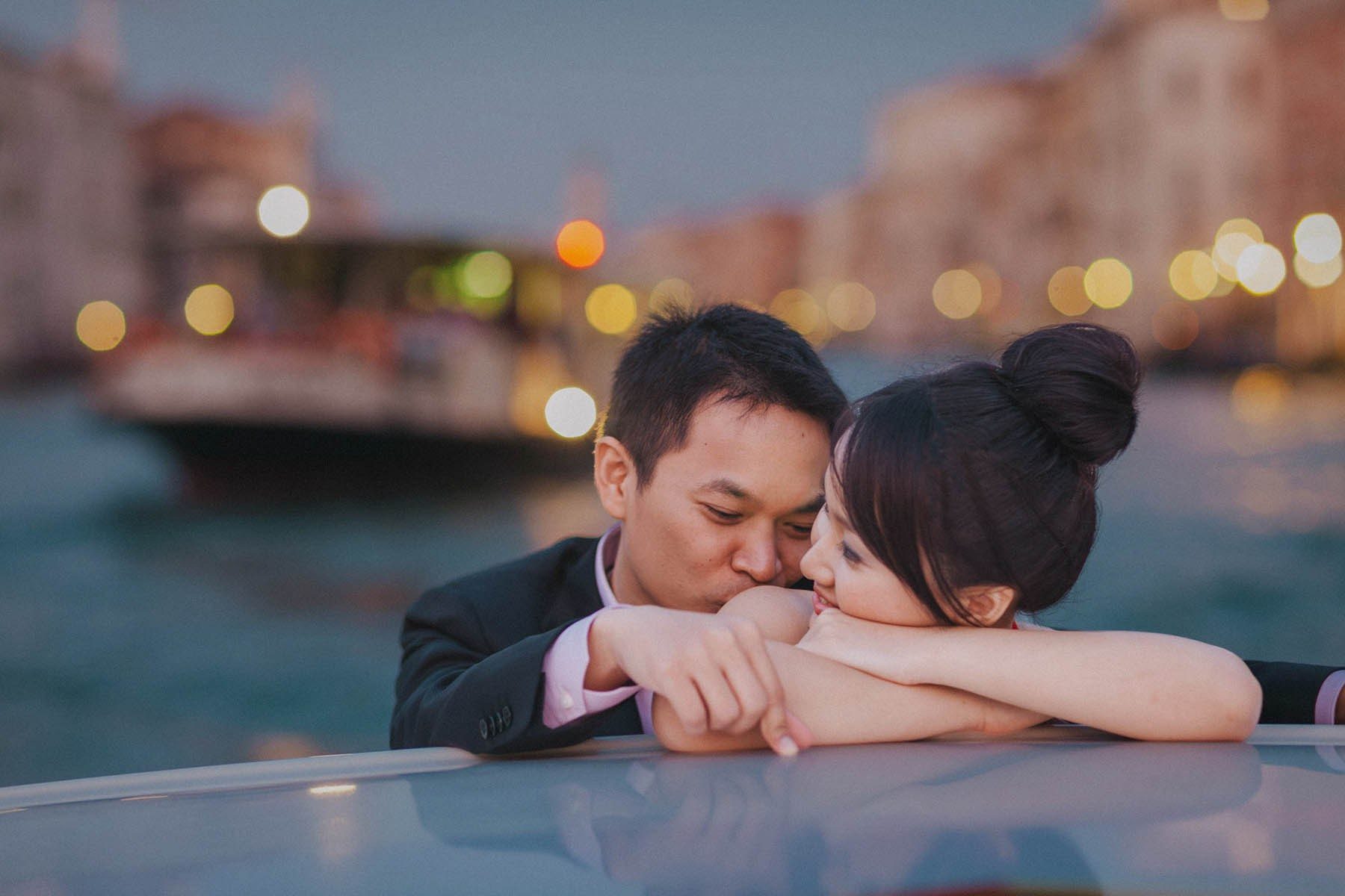 Smiling Thai woman embraced by groom during their private canal cruise in Venice.